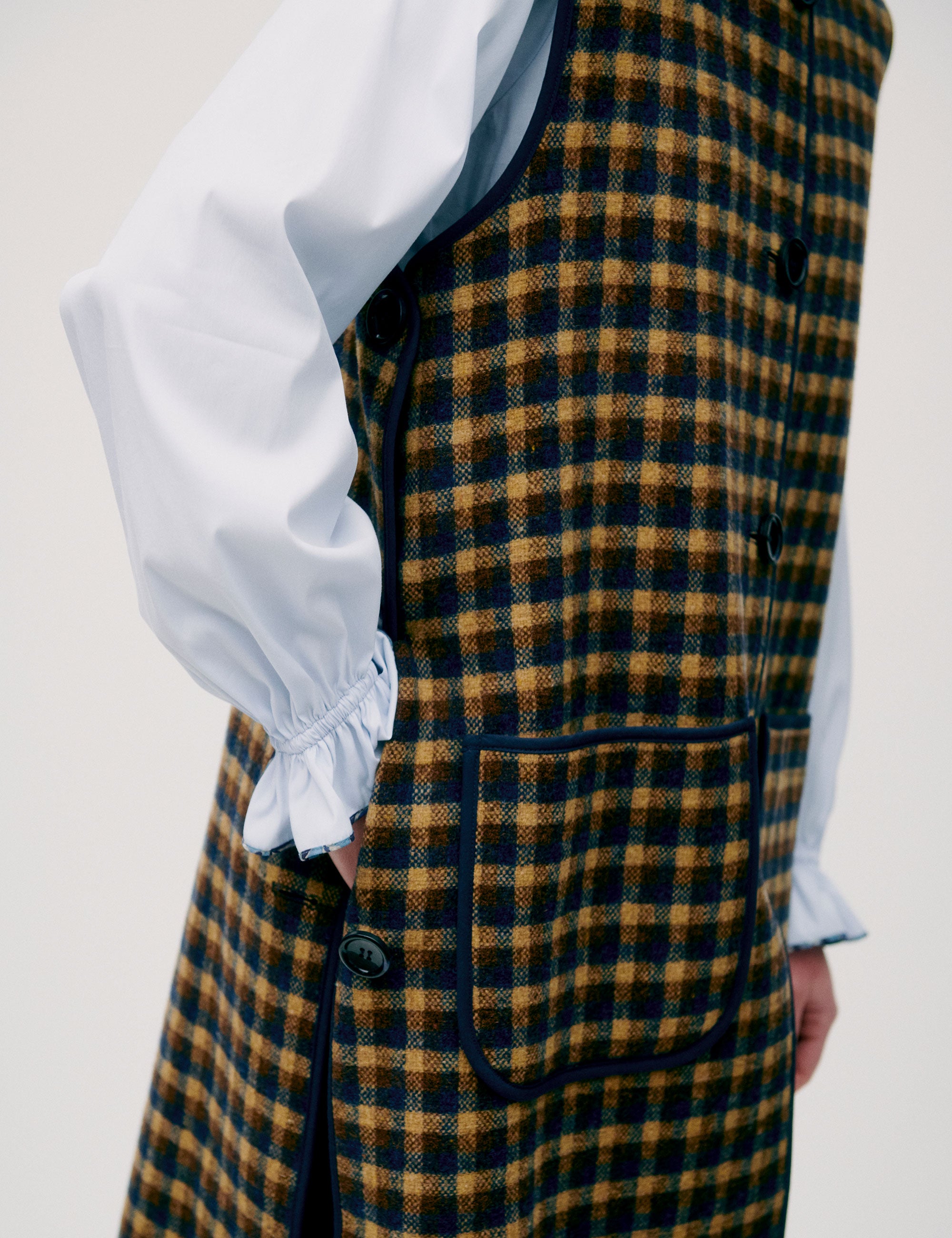 Woman in light blue shirt and long check patterned vest in yellow and black