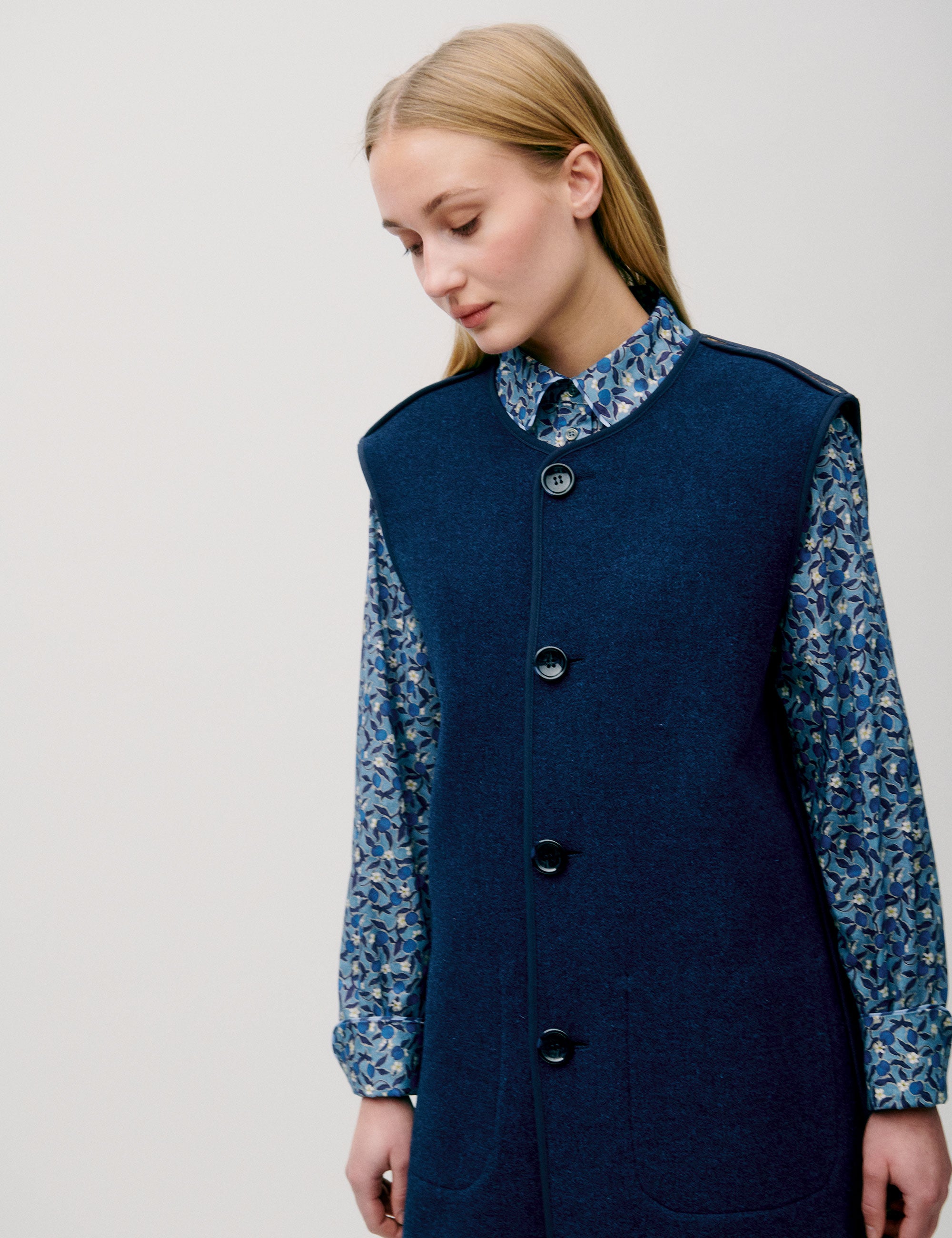 Woman in flower patterned long sleeved blue dress and long sleeveless wool vest with large buttons