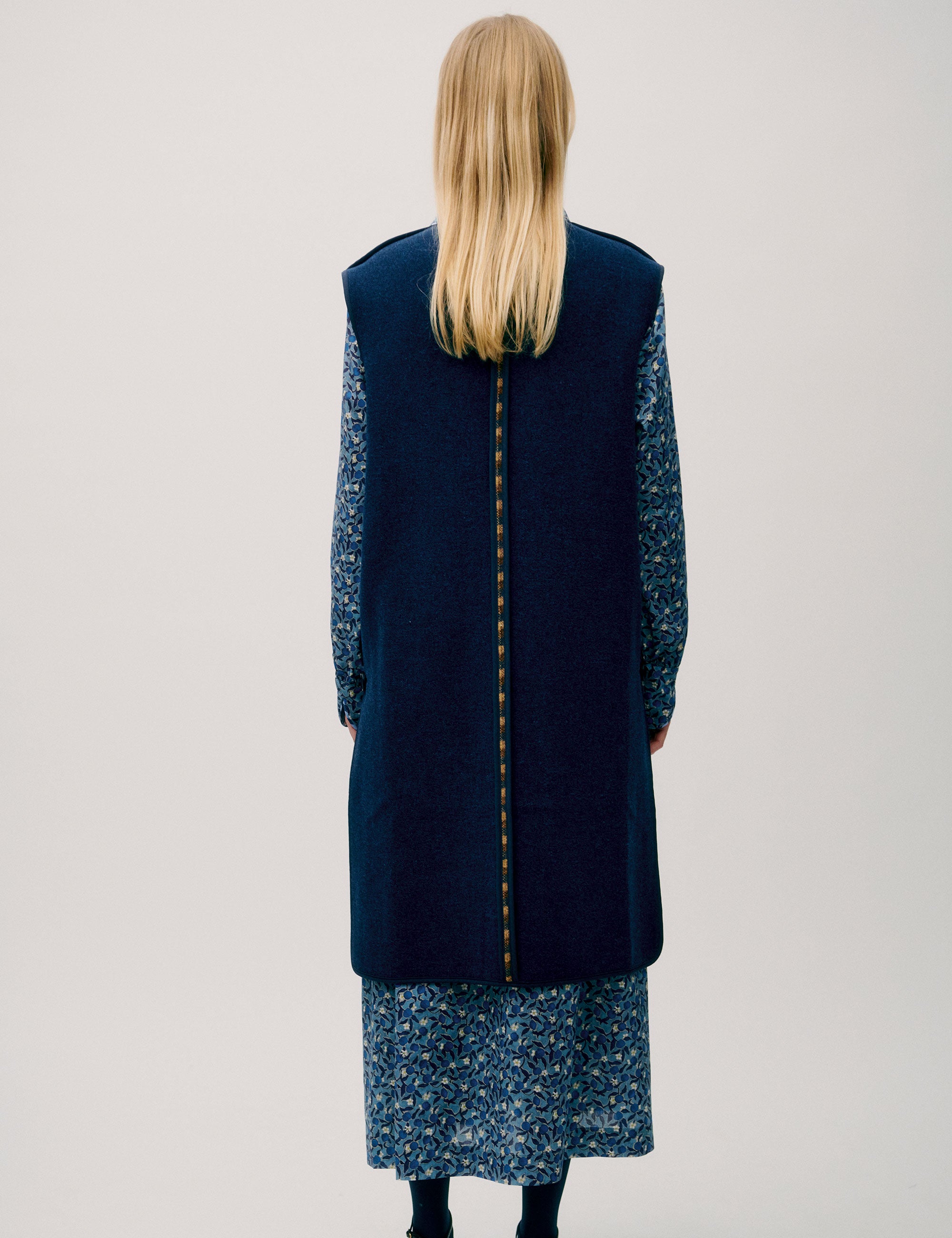 Woman in flower patterned long sleeved blue dress and long blue wool vest with large buttons