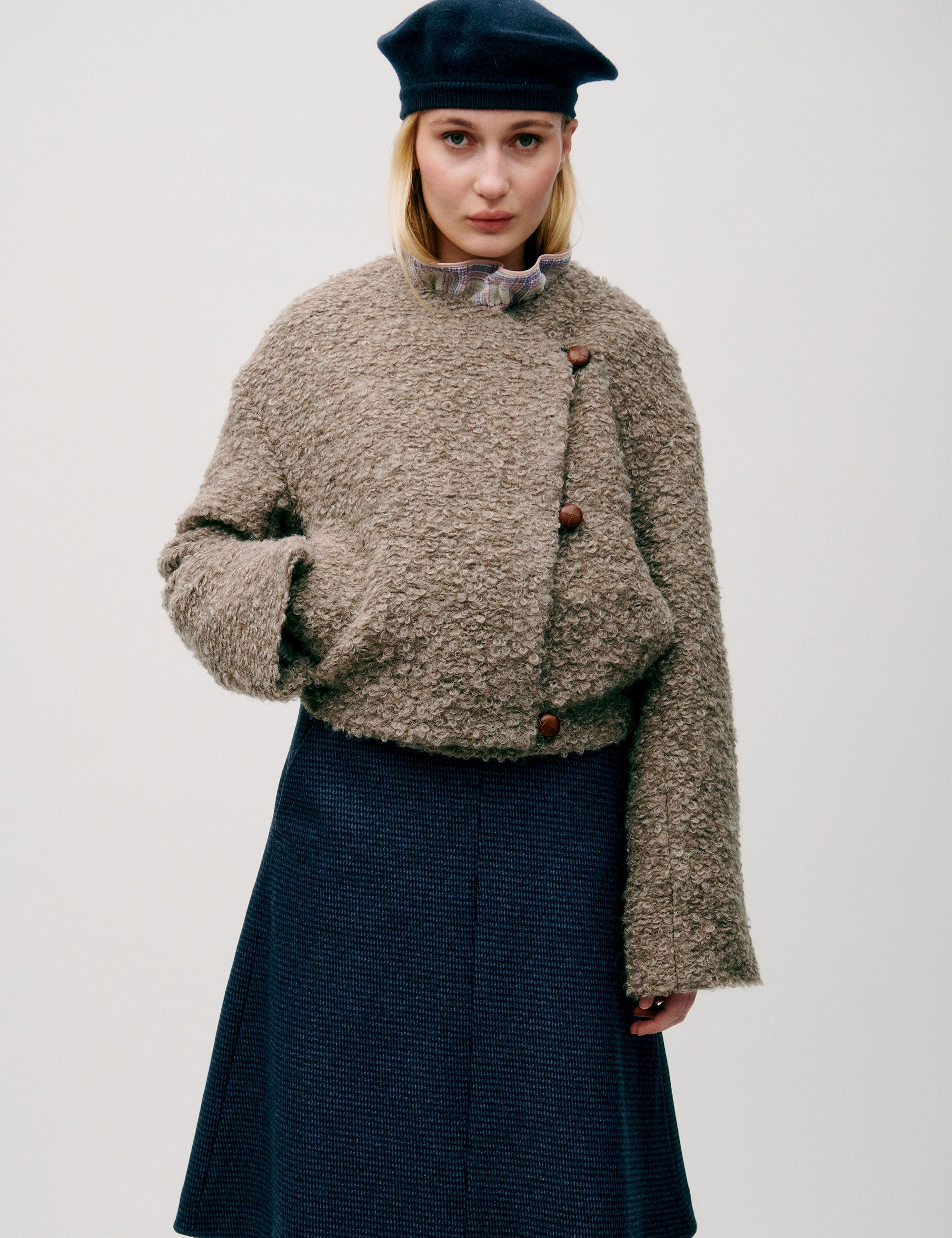 Woman in short wool jacket with assymetric design 3 buttons and a bubbly texture, blue skirt and beret