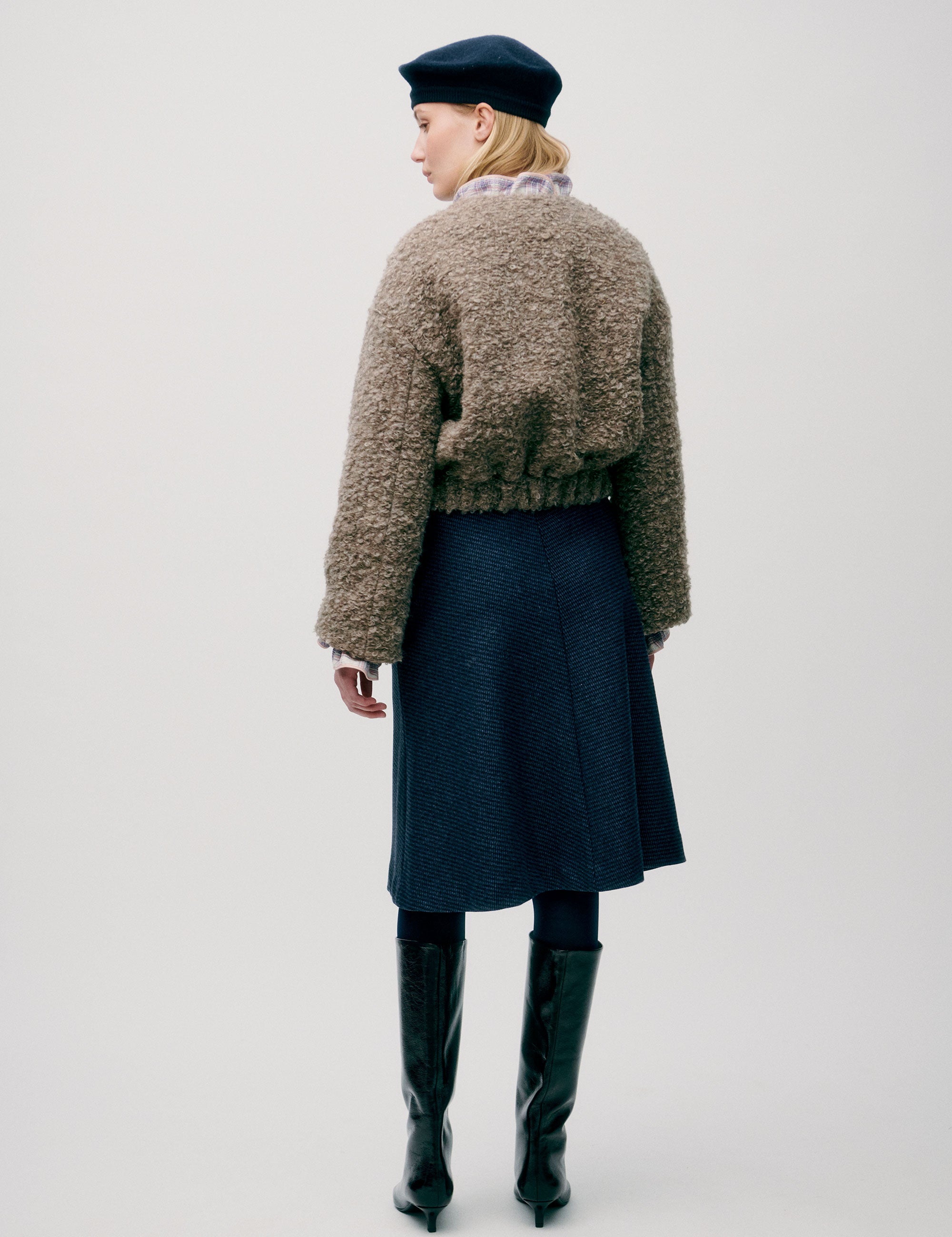 Woman in short wool jacket with assymetric design 3 buttons and a bubbly texture, blue skirt and beret