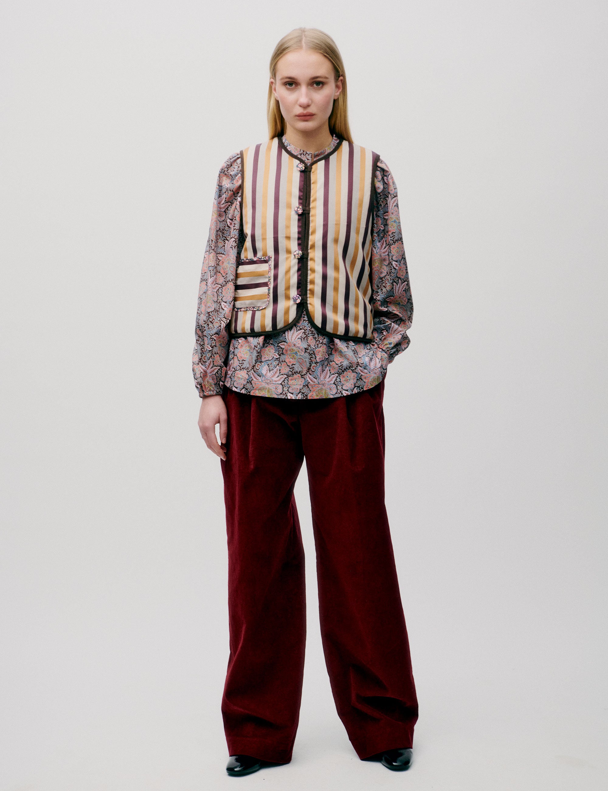 Woman in red trousers, flower paisley patternedblouse and yellow white and red striped vest