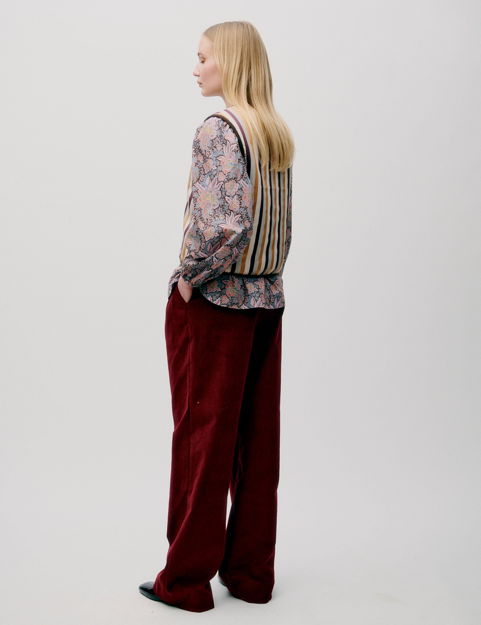 Woman in red trousers, flower paisley patternedblouse and yellow white and red striped vest