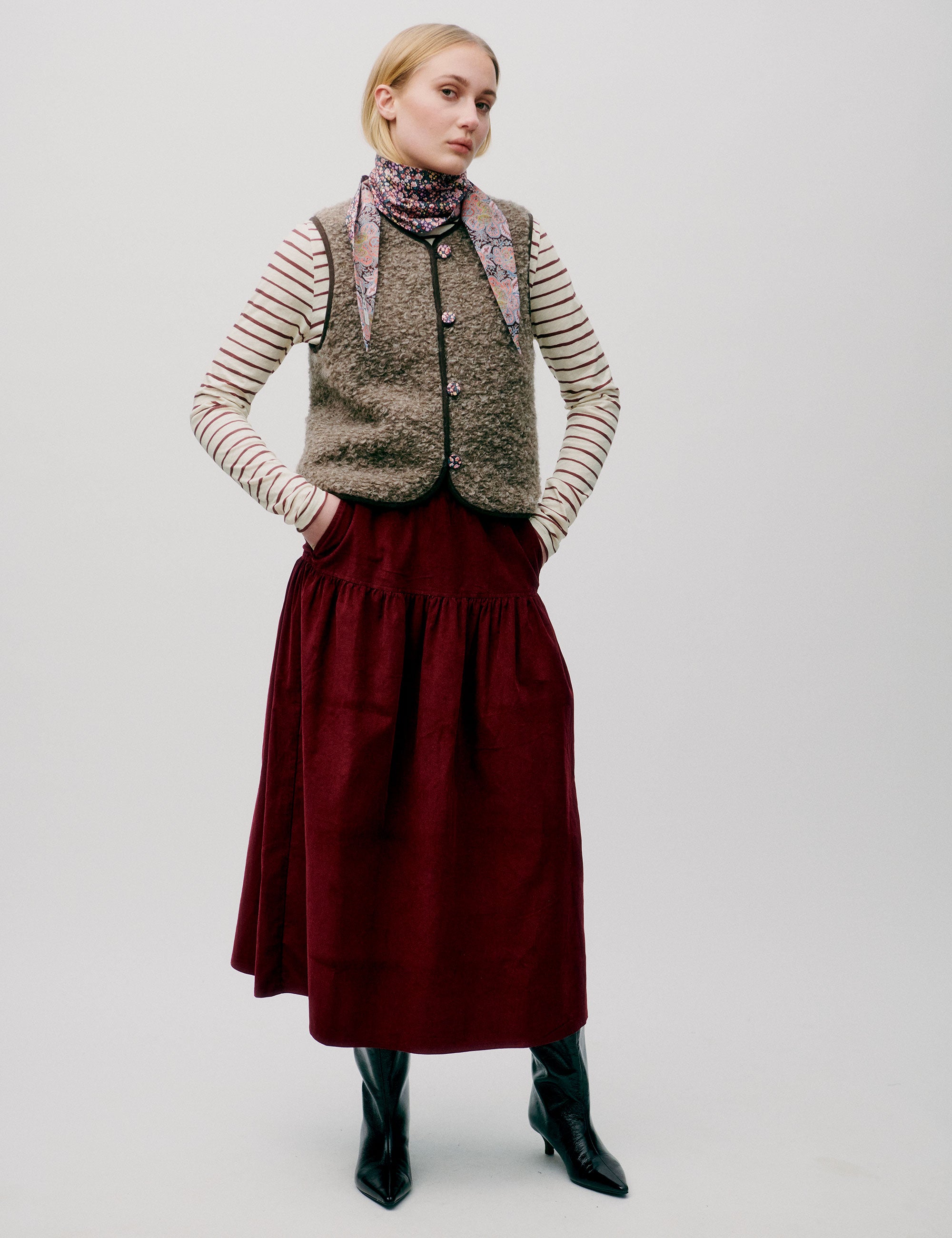 Woman in red corduroy skirt, striped long sleeved t-shirt and wool vest with buttons and lining