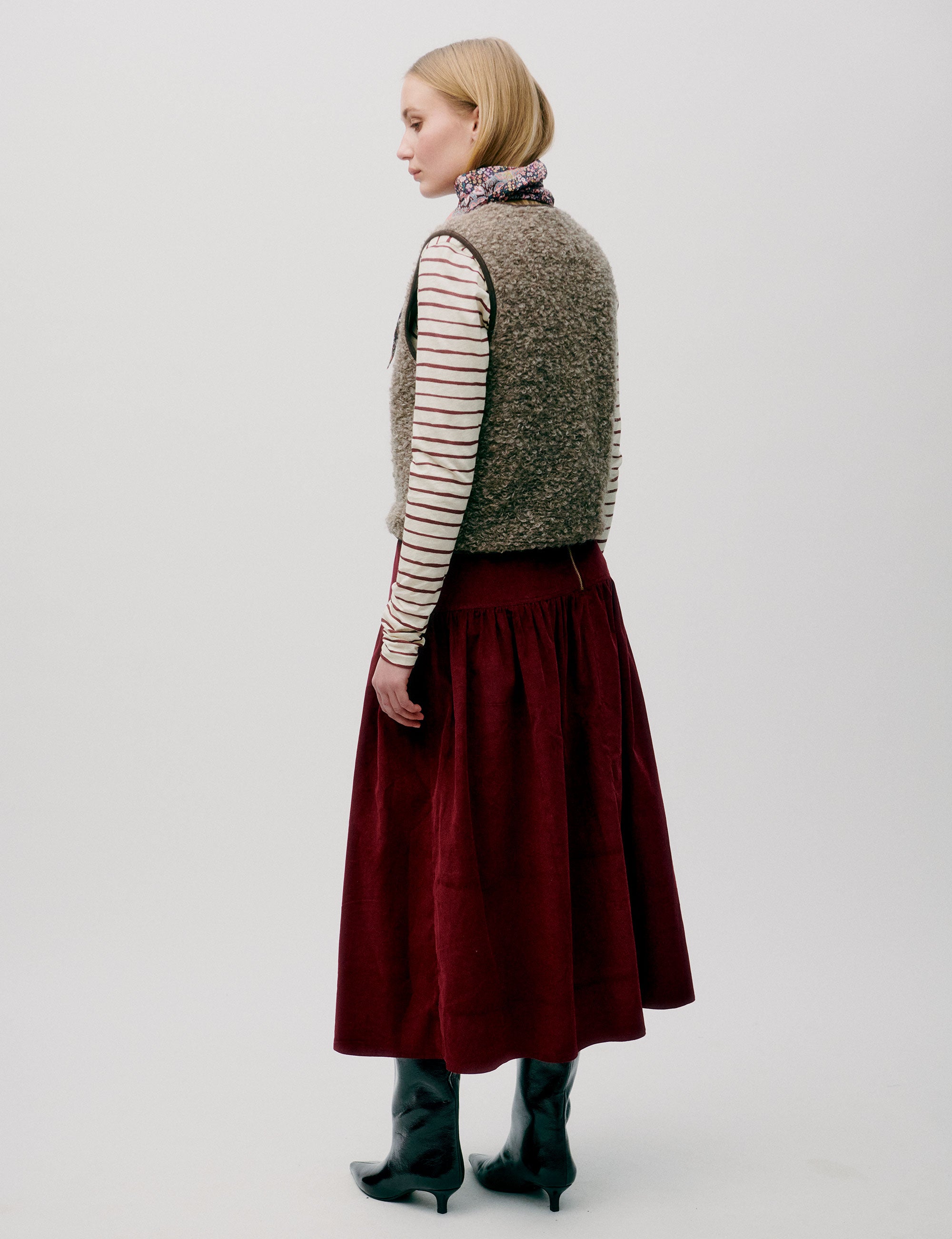 Woman in red corduroy skirt, striped long sleeved t-shirt and wool vest with buttons and lining