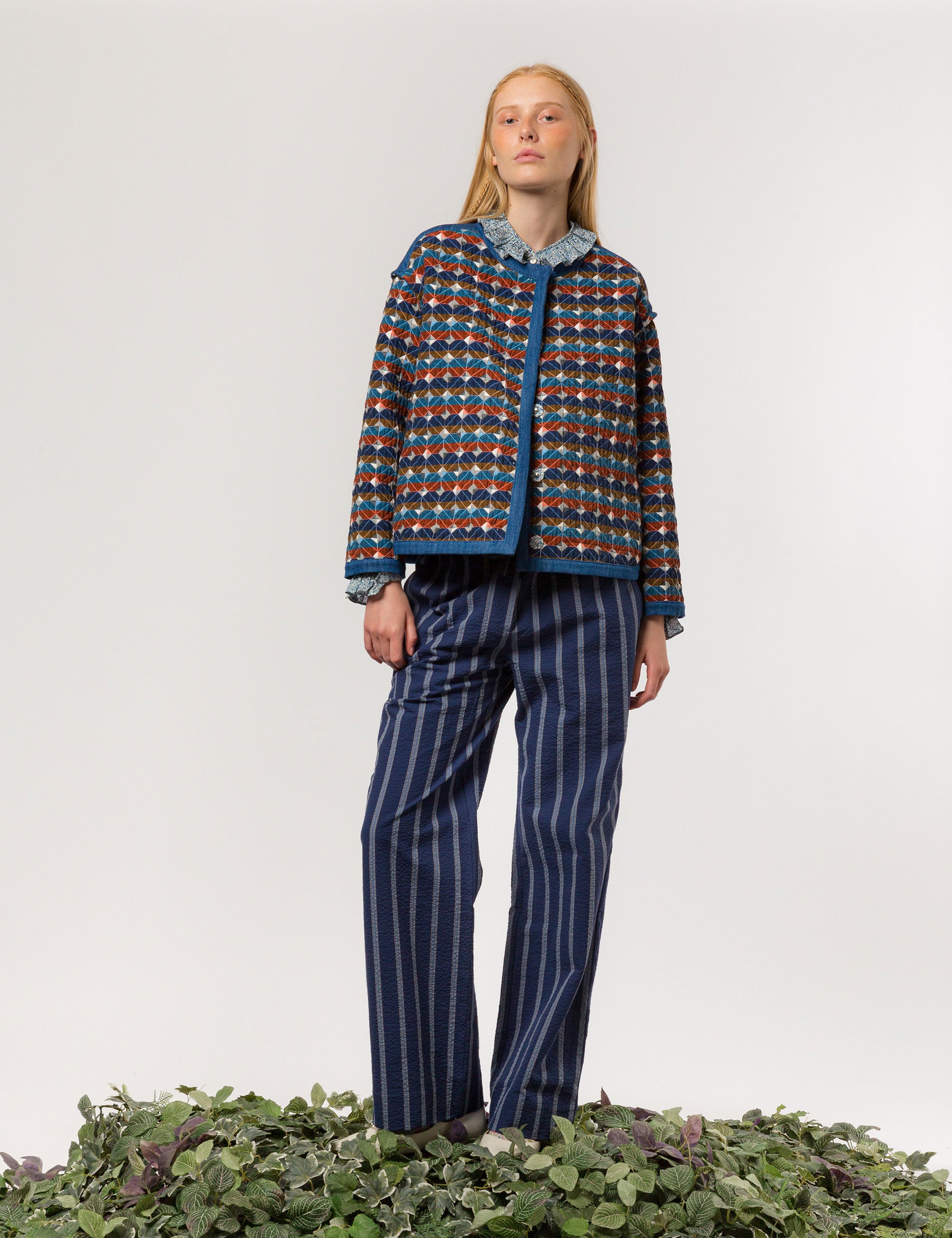 Woman in blue and white striped wide and relaxed seersucker pants frilled shirt and quilt jacket with multi-colored checked pattern