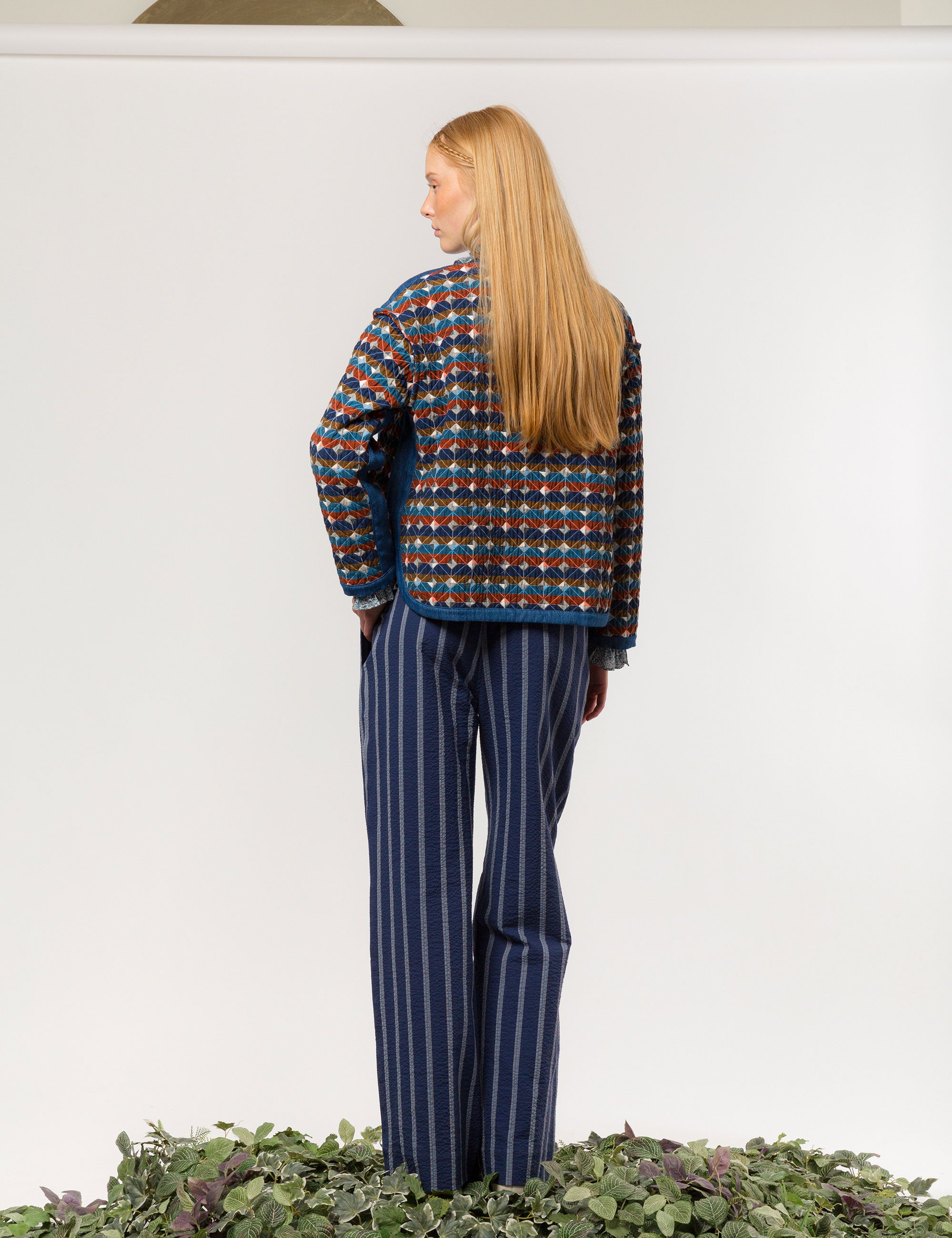 Woman in blue and white striped wide and relaxed seersucker pants frilled shirt and quilted jacket with multi-colored checked pattern