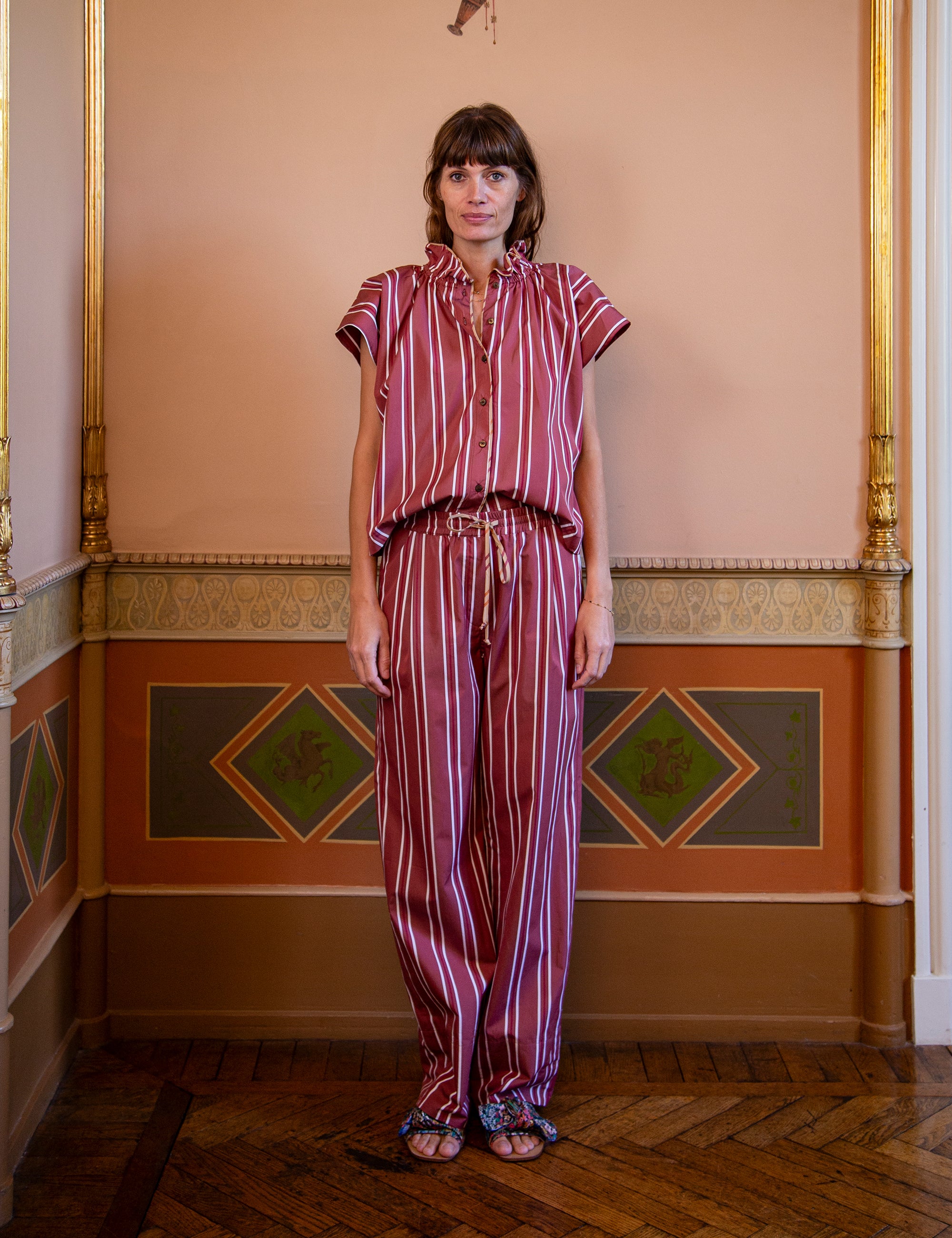 Woman wearing a striped outfit standing in an ornate room with decorative walls.