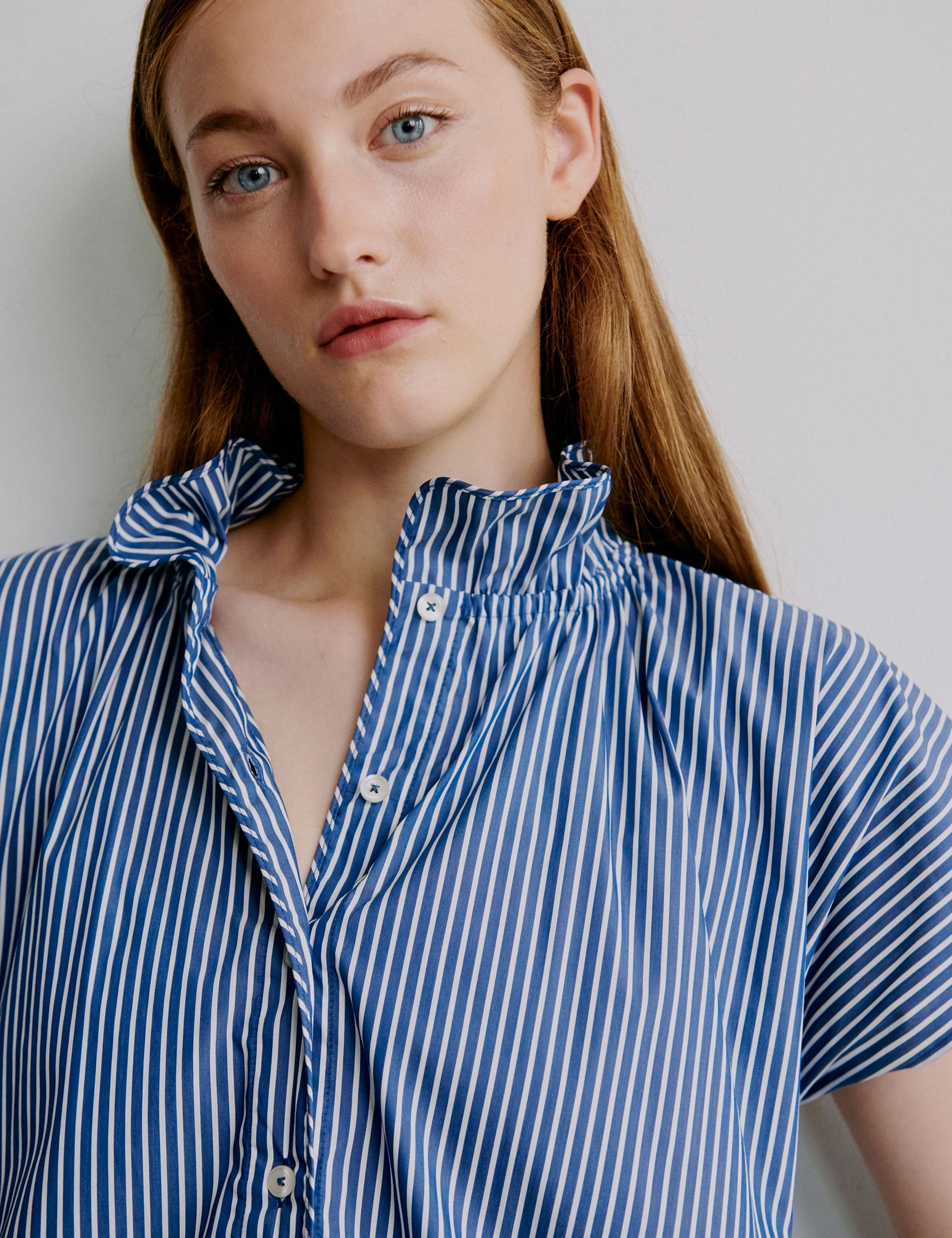 Woman wearing a blue and white striped shirt with buttons and frilled collar