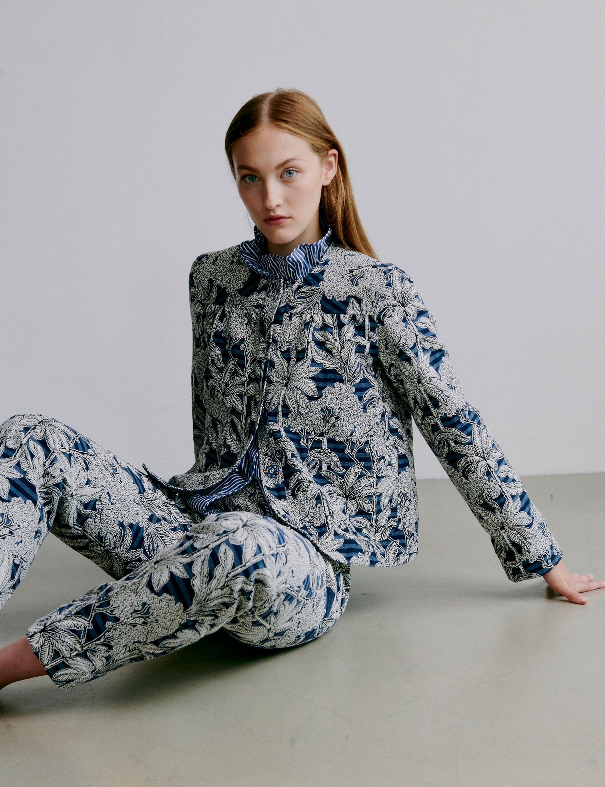 Woman wearing a blue floral jacket and pants set sitting on a light-colored floor.