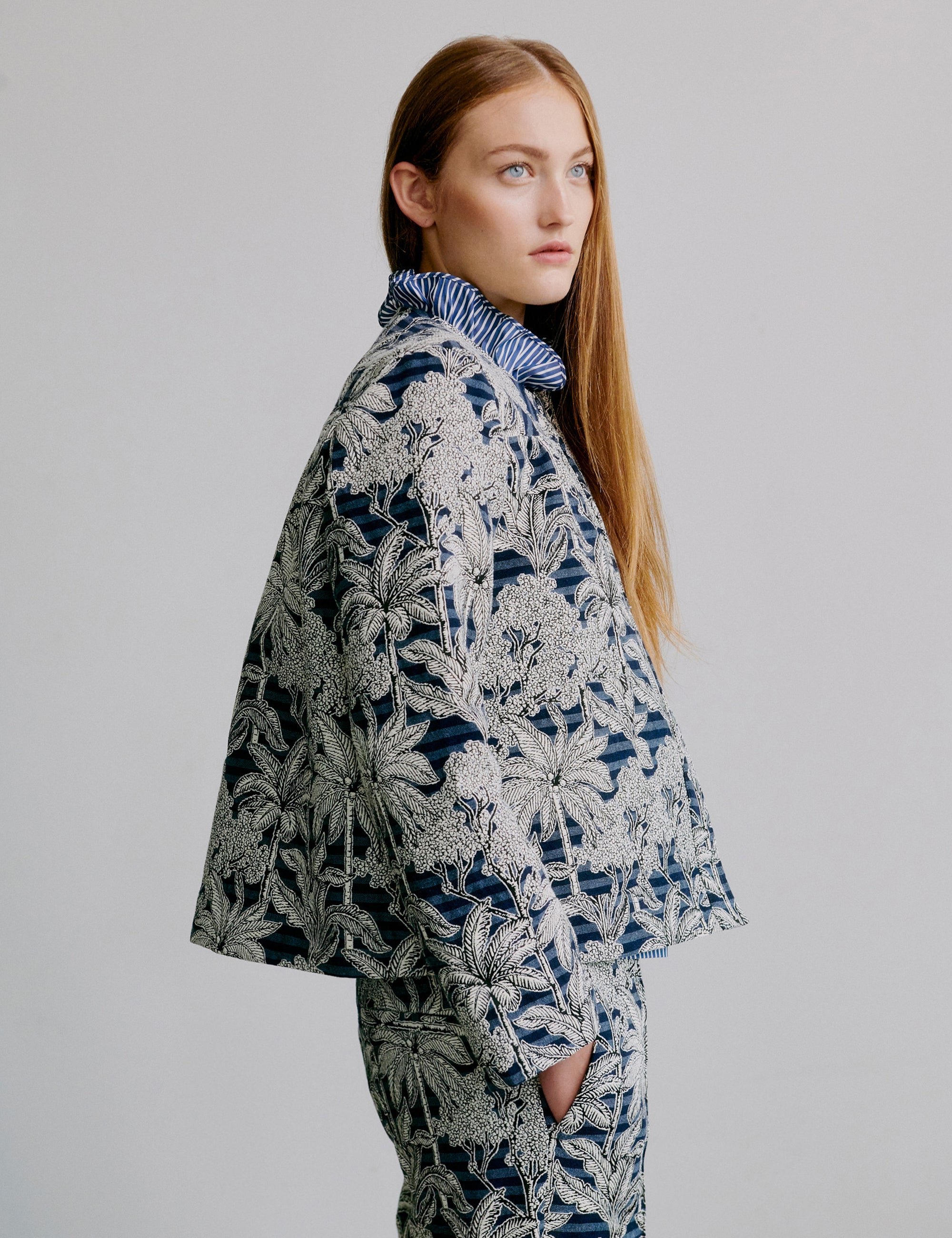 Woman wearing a blue floral patterned jacket with matching pants on a plain background