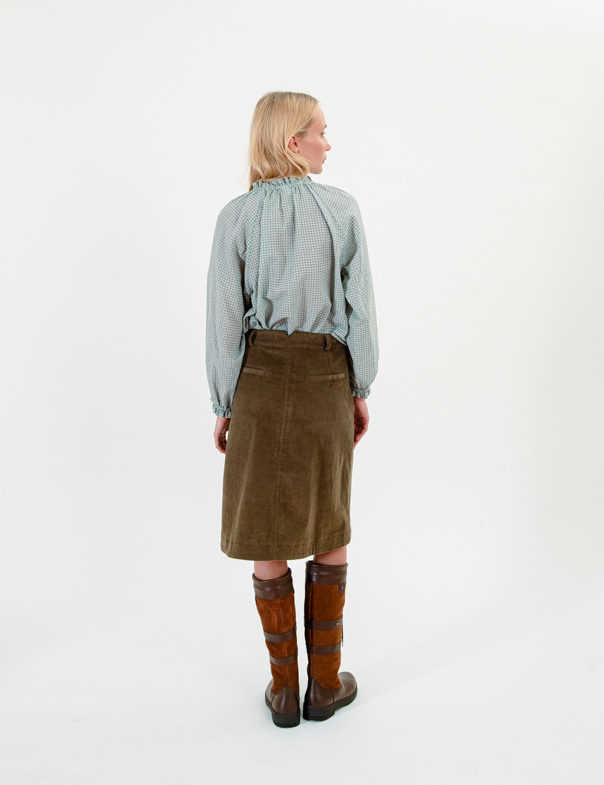 Person wearing a green checkered blouse, green skirt, and brown knee-high boots on a white background