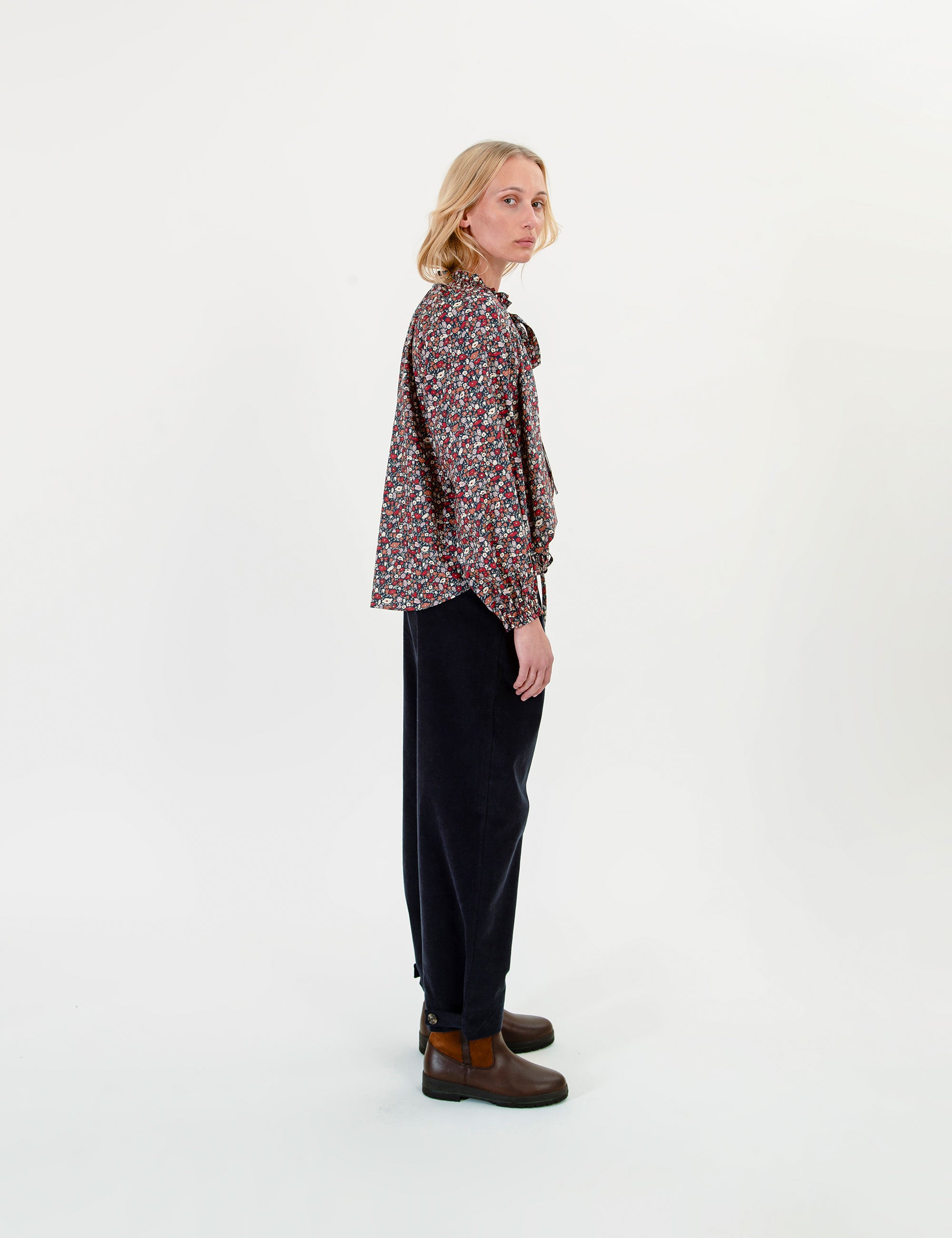 Woman wearing a patterned blouse and dark pants on a white background