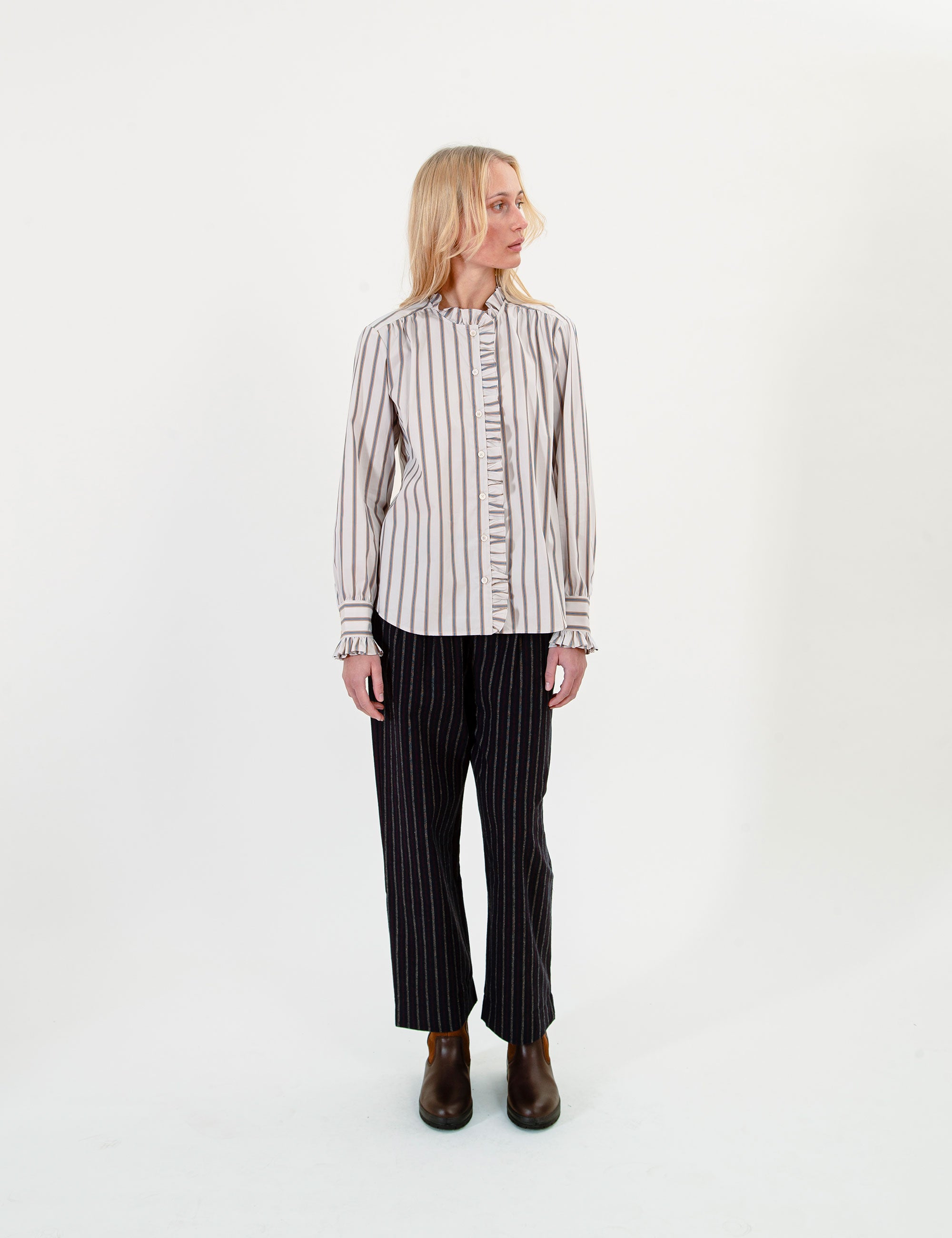 Woman wearing a striped ruffled shirt and black pants on a white background