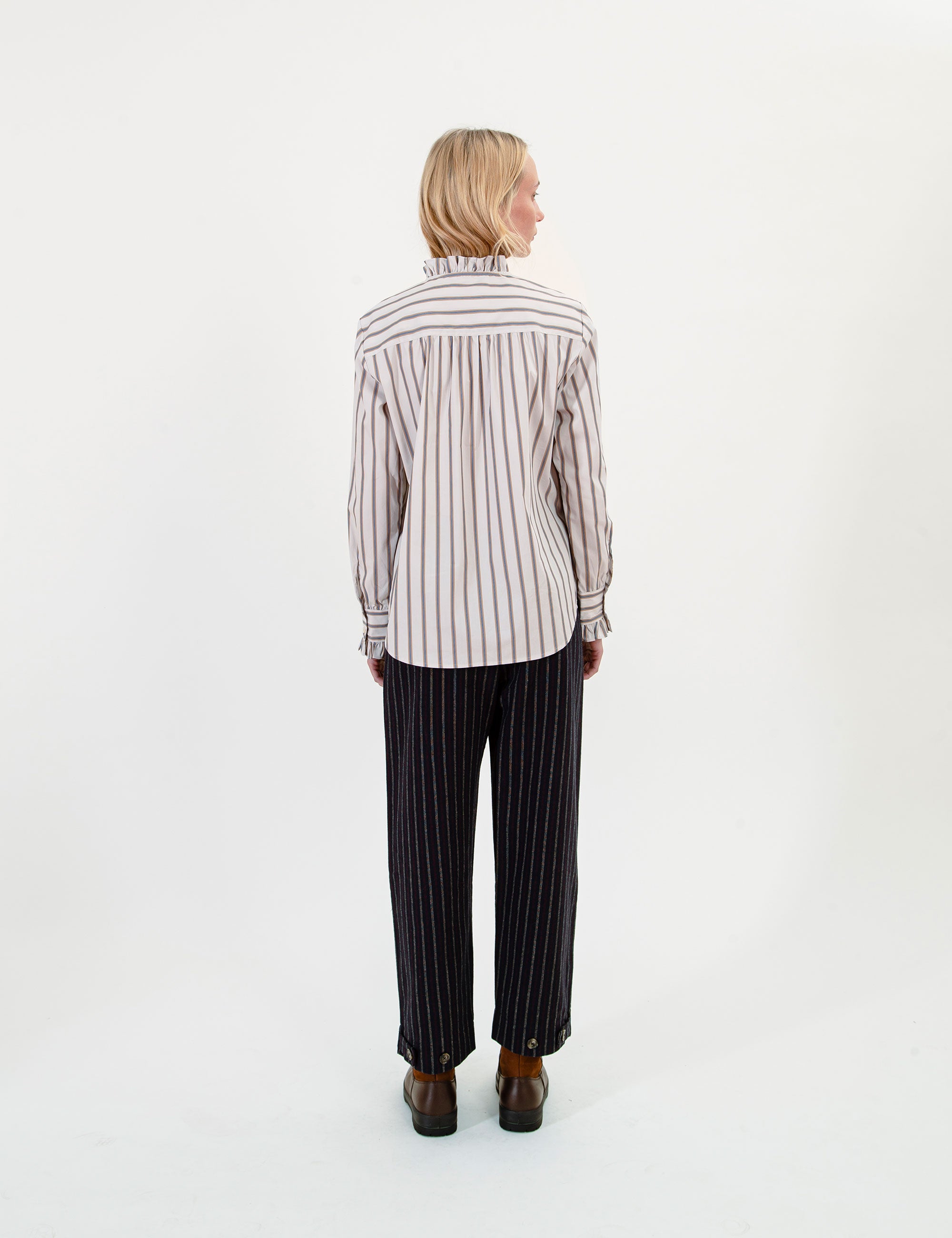 Woman wearing a striped ruffled shirt and black pants on a white background