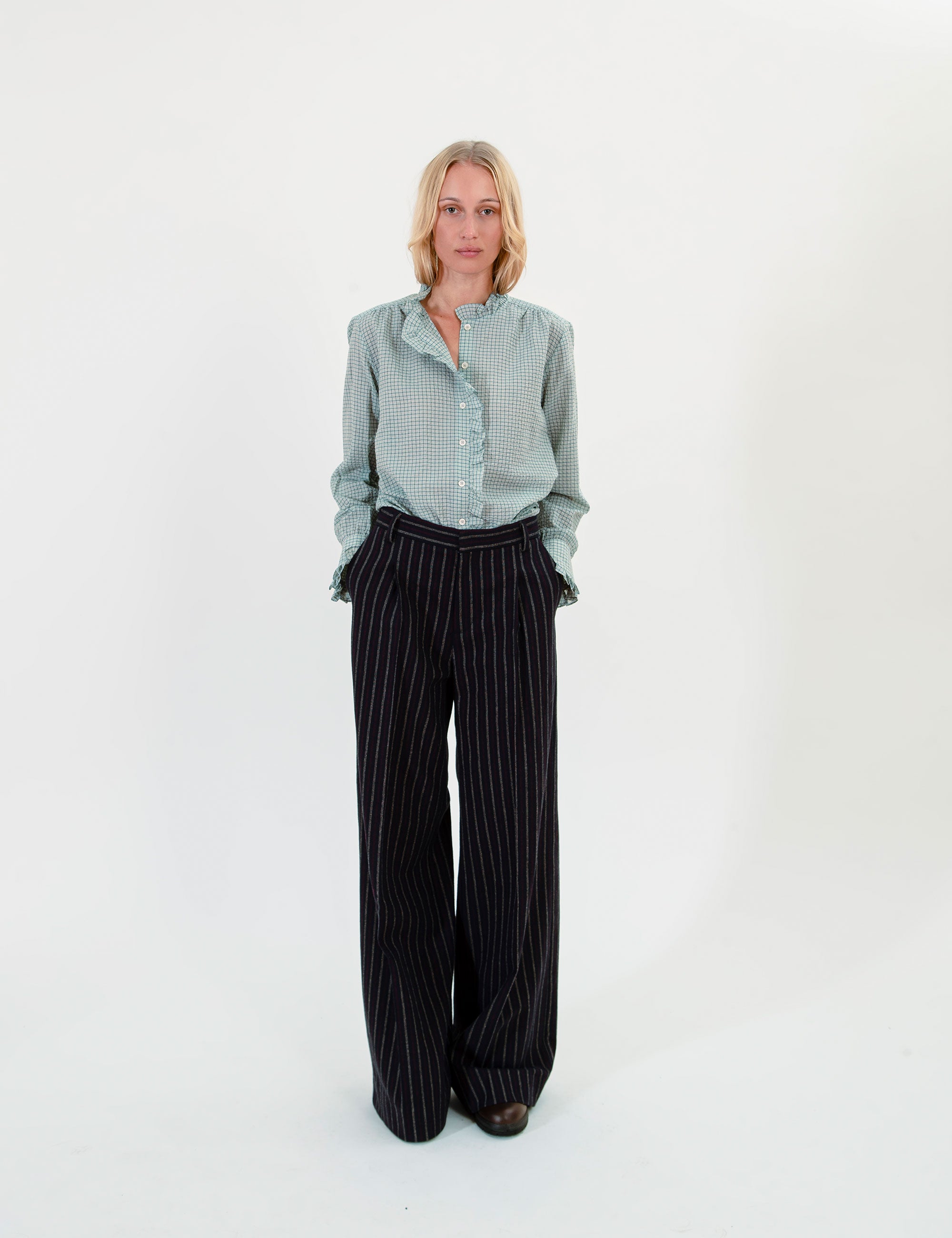 Woman wearing a light green ruffled shirt and black striped pants on a white background