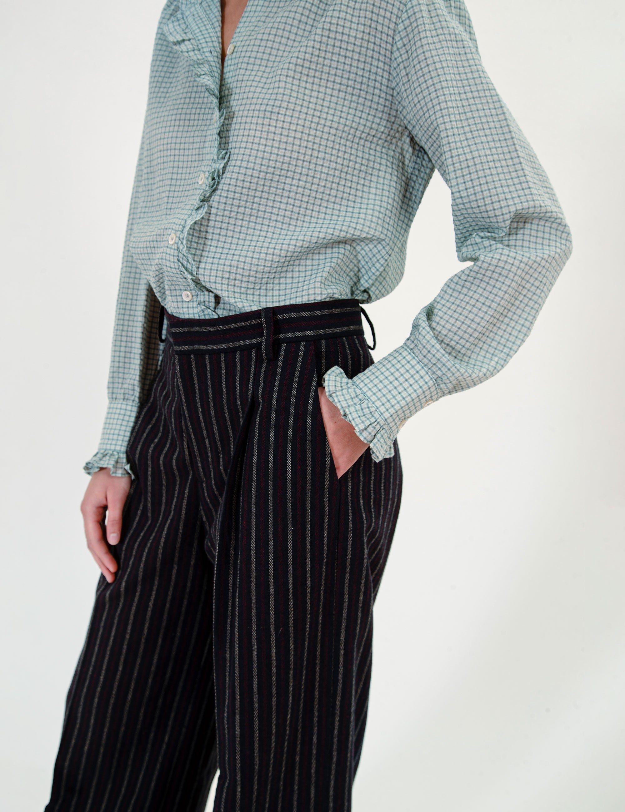 Woman wearing a light green checkered shirt and black striped pants on a white background