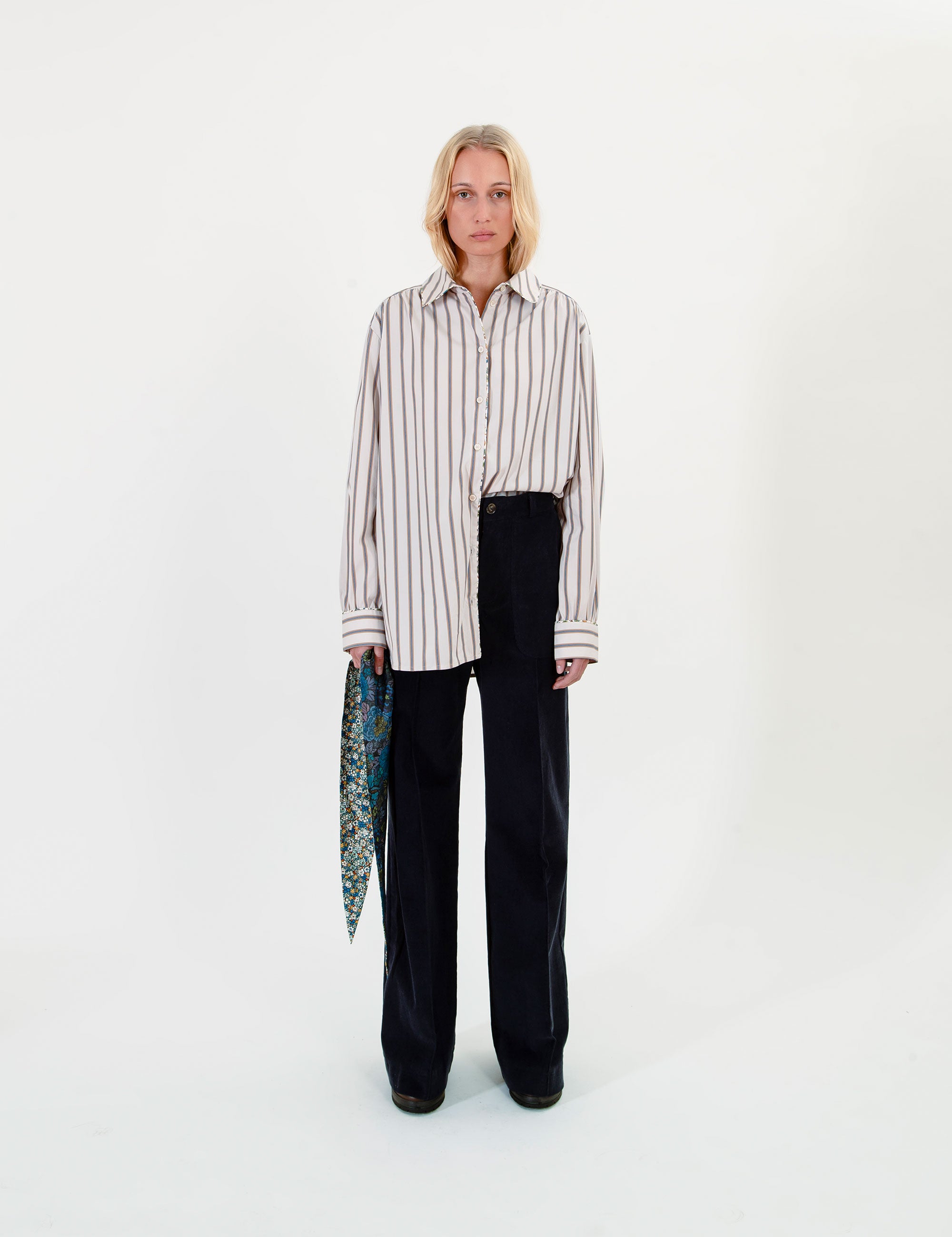Woman wearing a striped shirt and black pants holding a patterned scarf on a white background