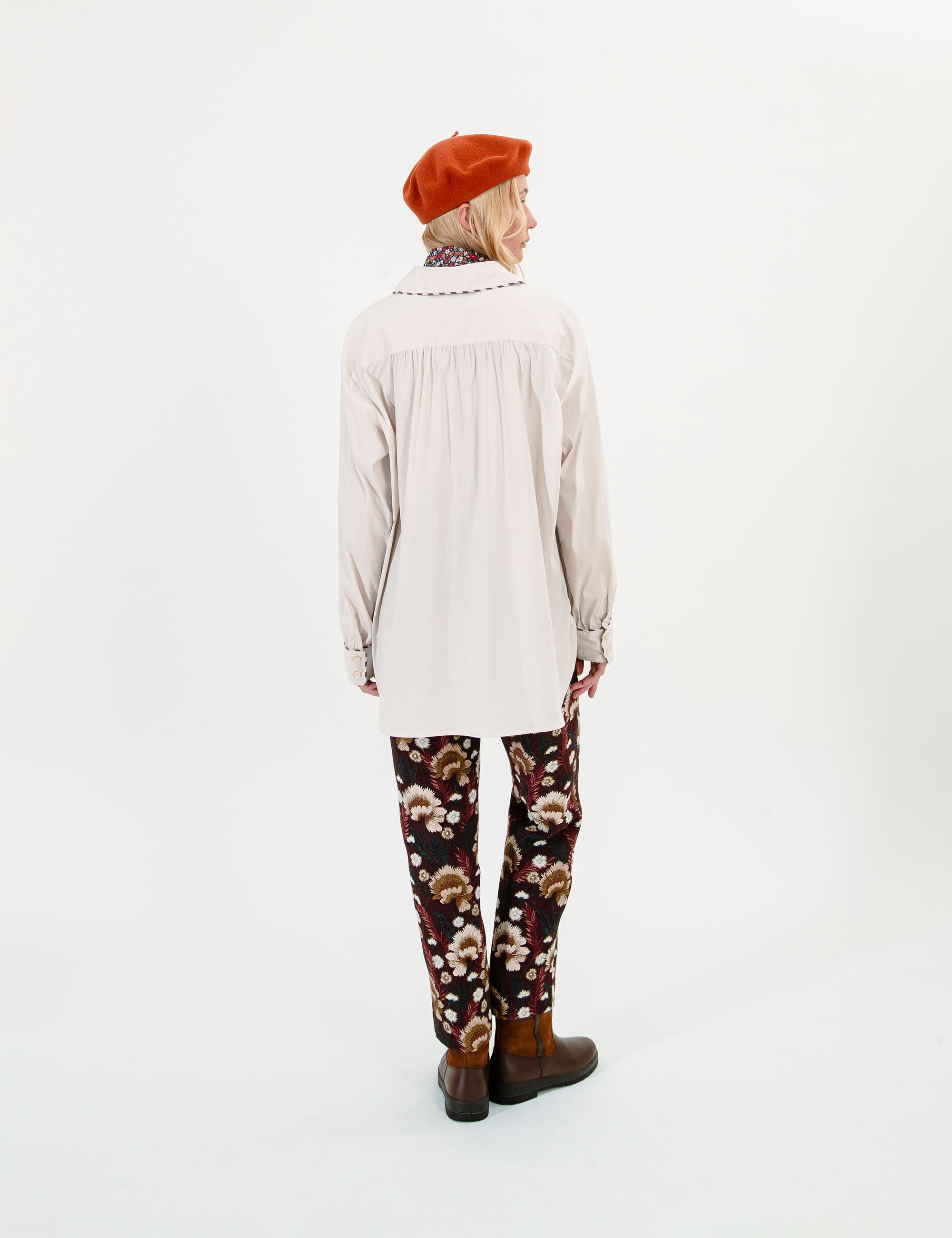 Woman wearing a beige shirt and brown floral pants on a white background