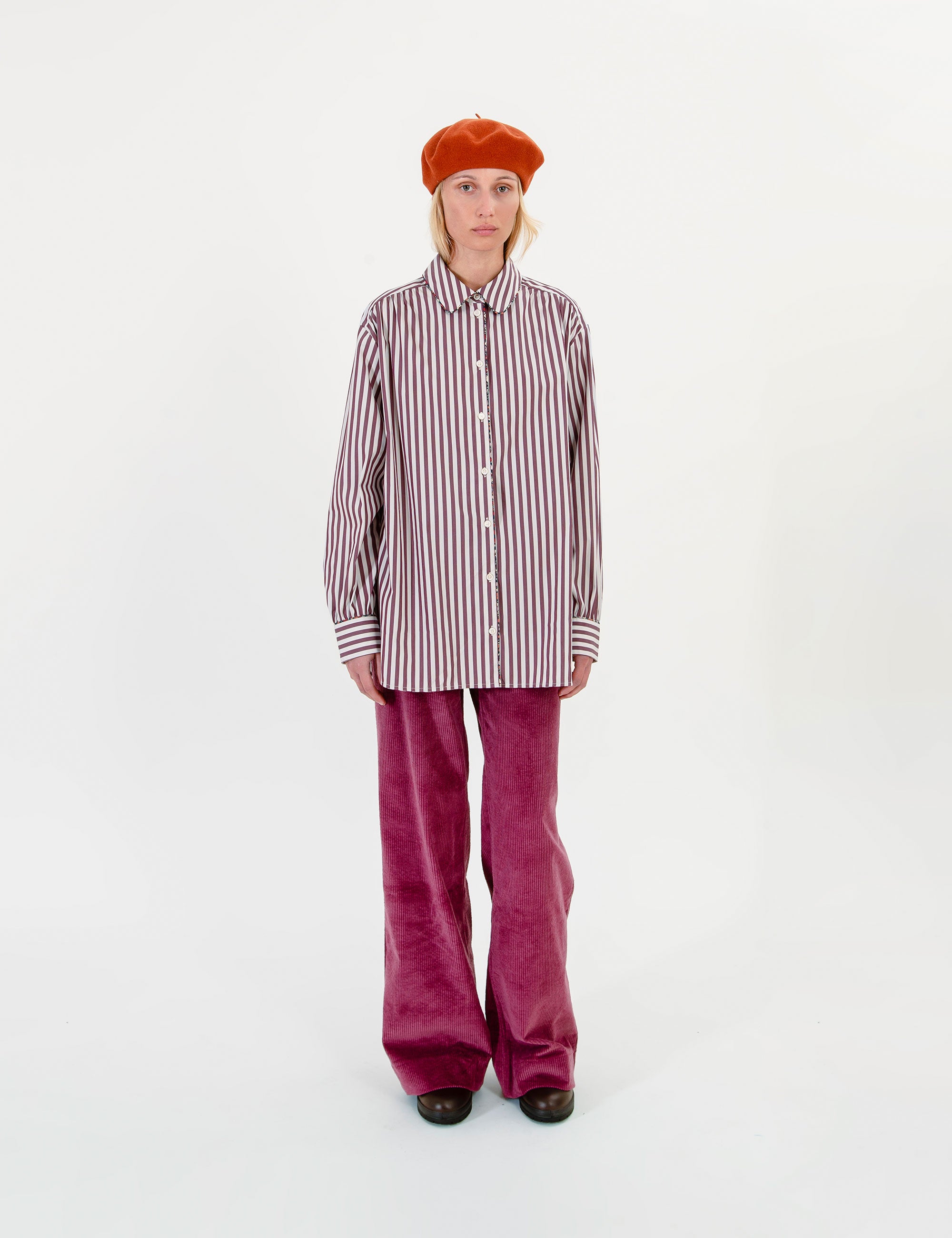 Woman wearing a striped shirt, orange beret, and pink pants on a white background