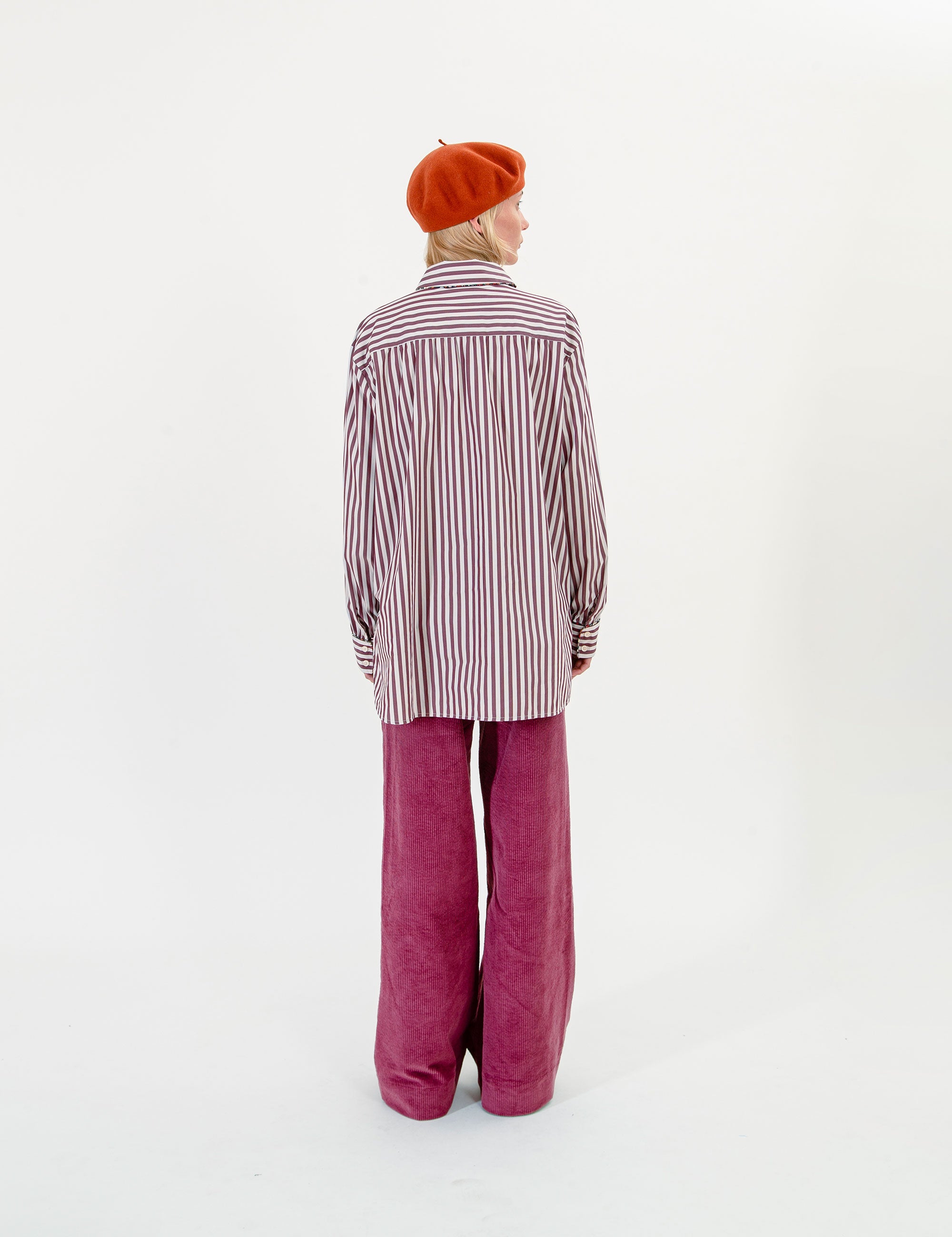 Woman wearing a striped shirt, orange beret, and pink pants on a white background