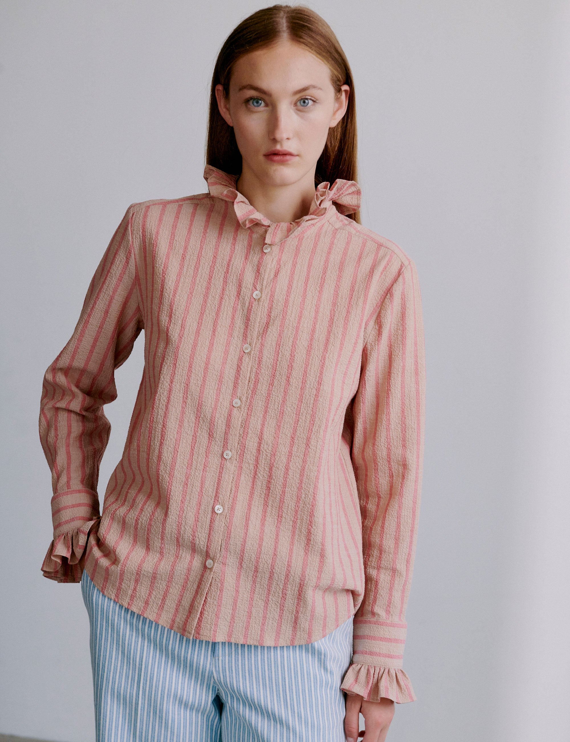 Woman wearing a pink and red striped seersucker shirt with ruffled sleeves and collar and light blue and white striped pants