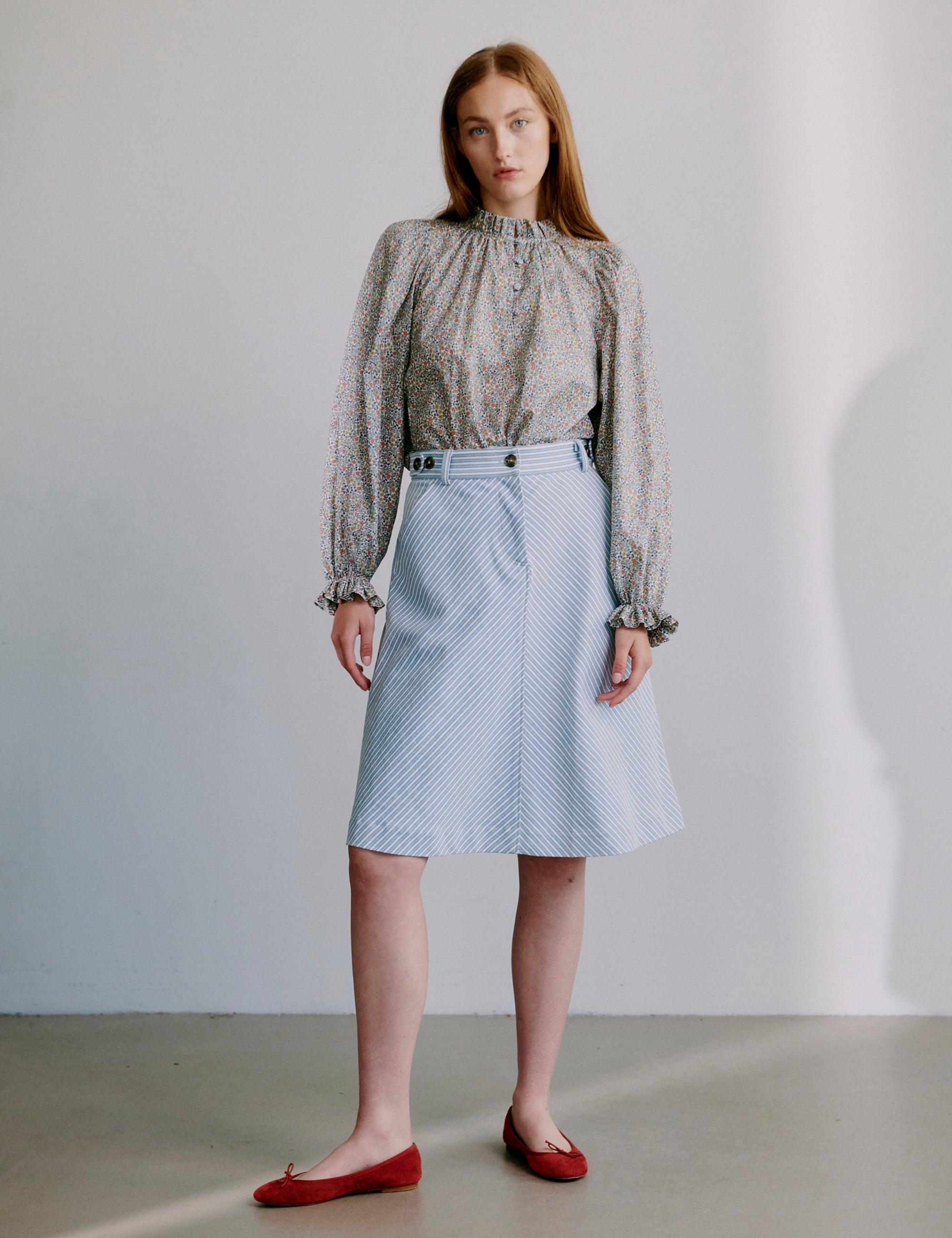 Woman wearing a floral patterned blouse and light blue skirt with red shoes