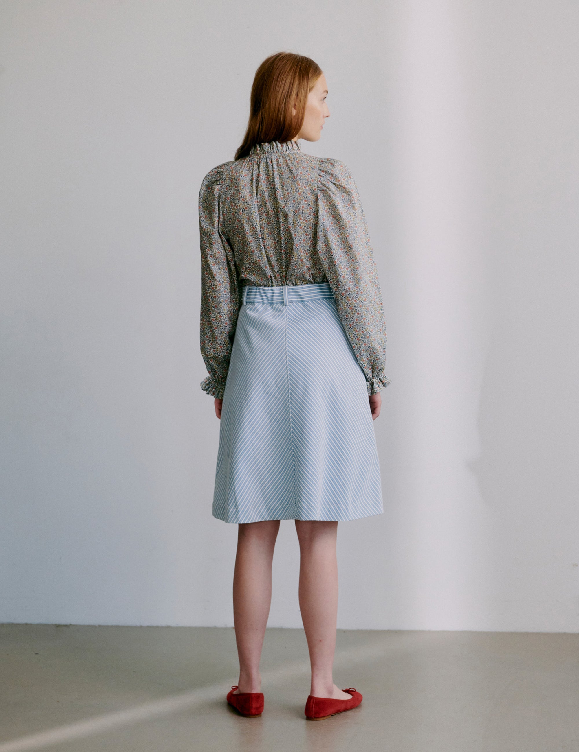 Woman wearing a floral patterned blouse and light blue skirt with red shoes