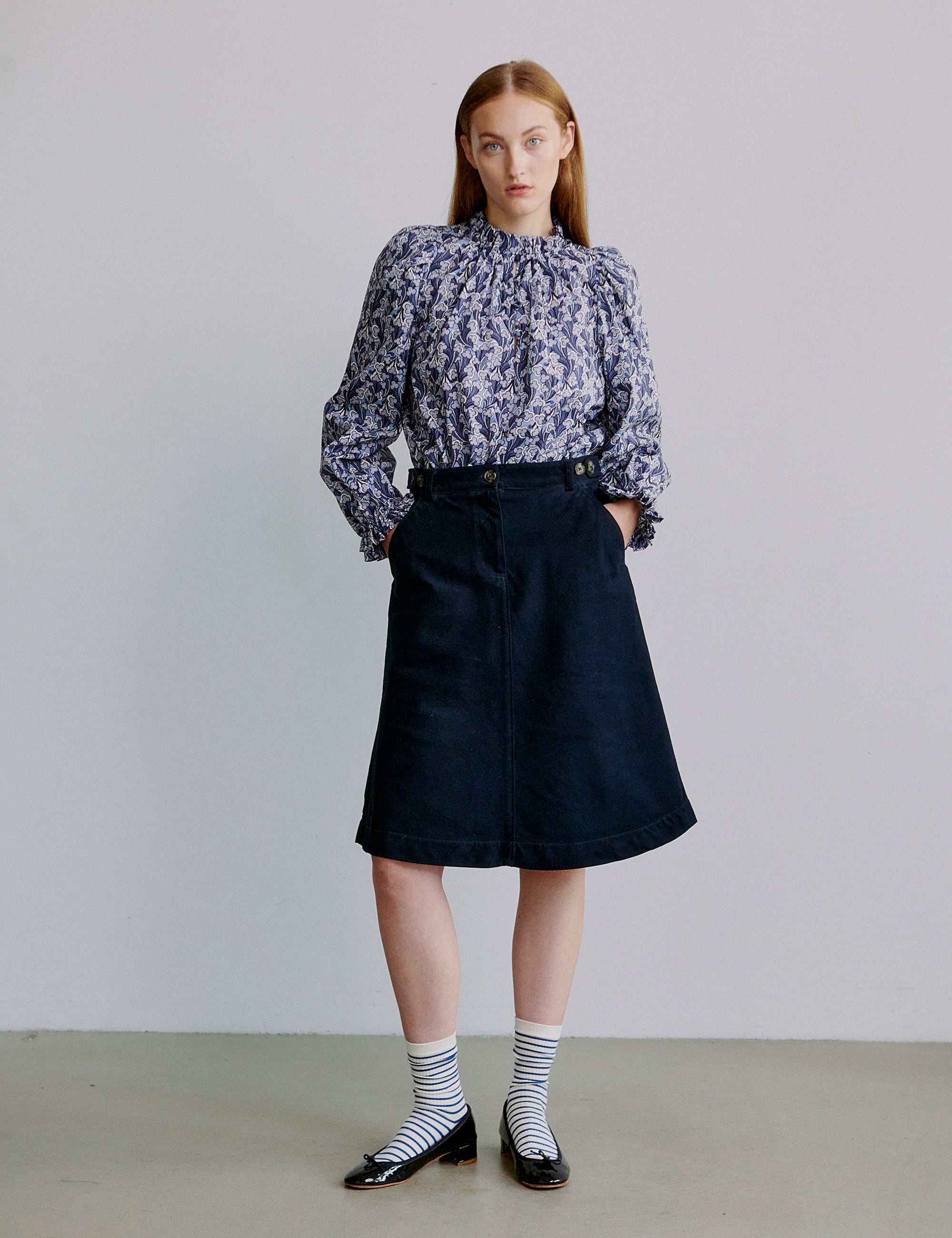 Woman wearing a floral blouse and blue skirt against a plain background