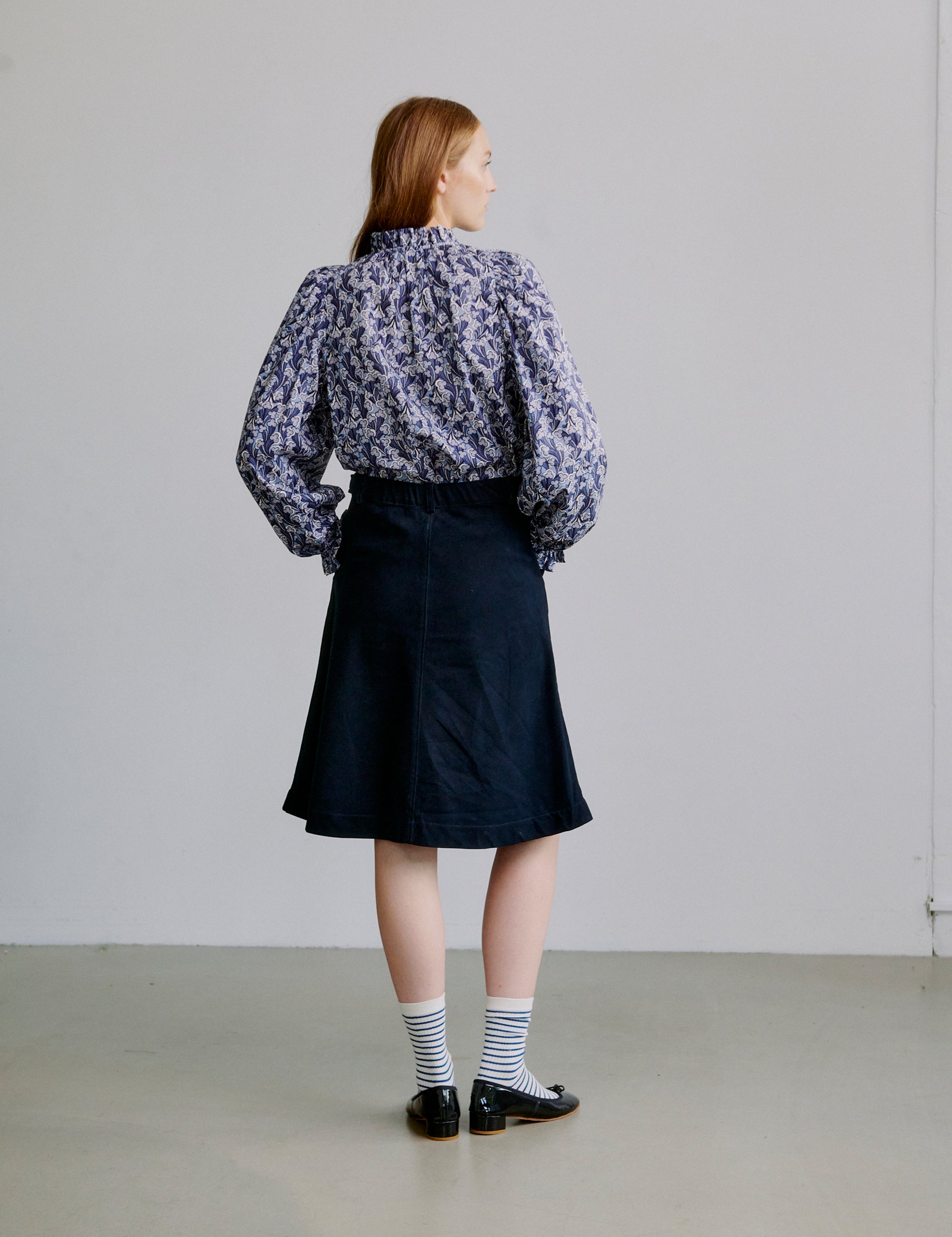 Woman wearing a floral blouse and blue skirt against a plain background