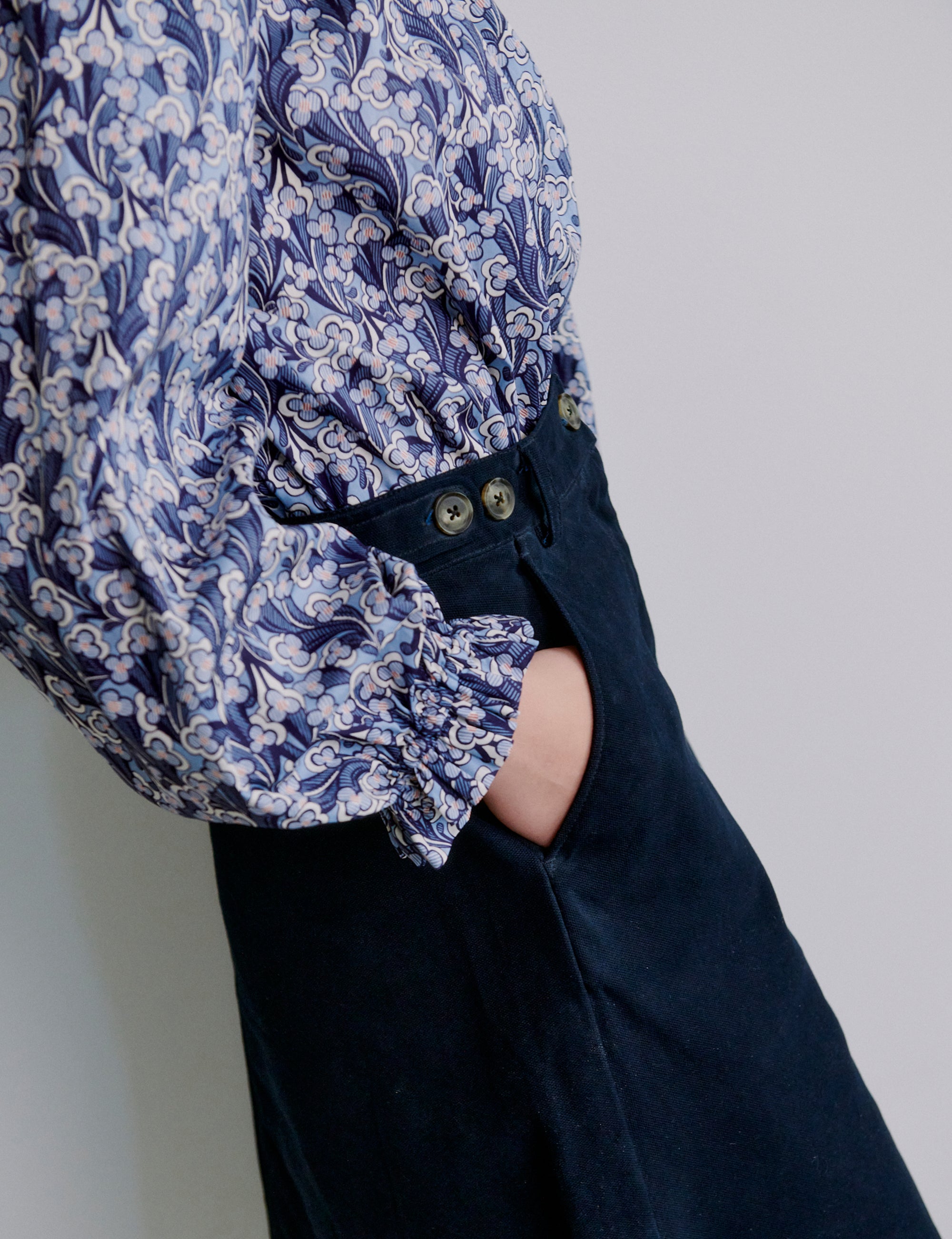 Woman wearing a blue and white patterned shirt with long puff sleeves and blue skirt with pockets