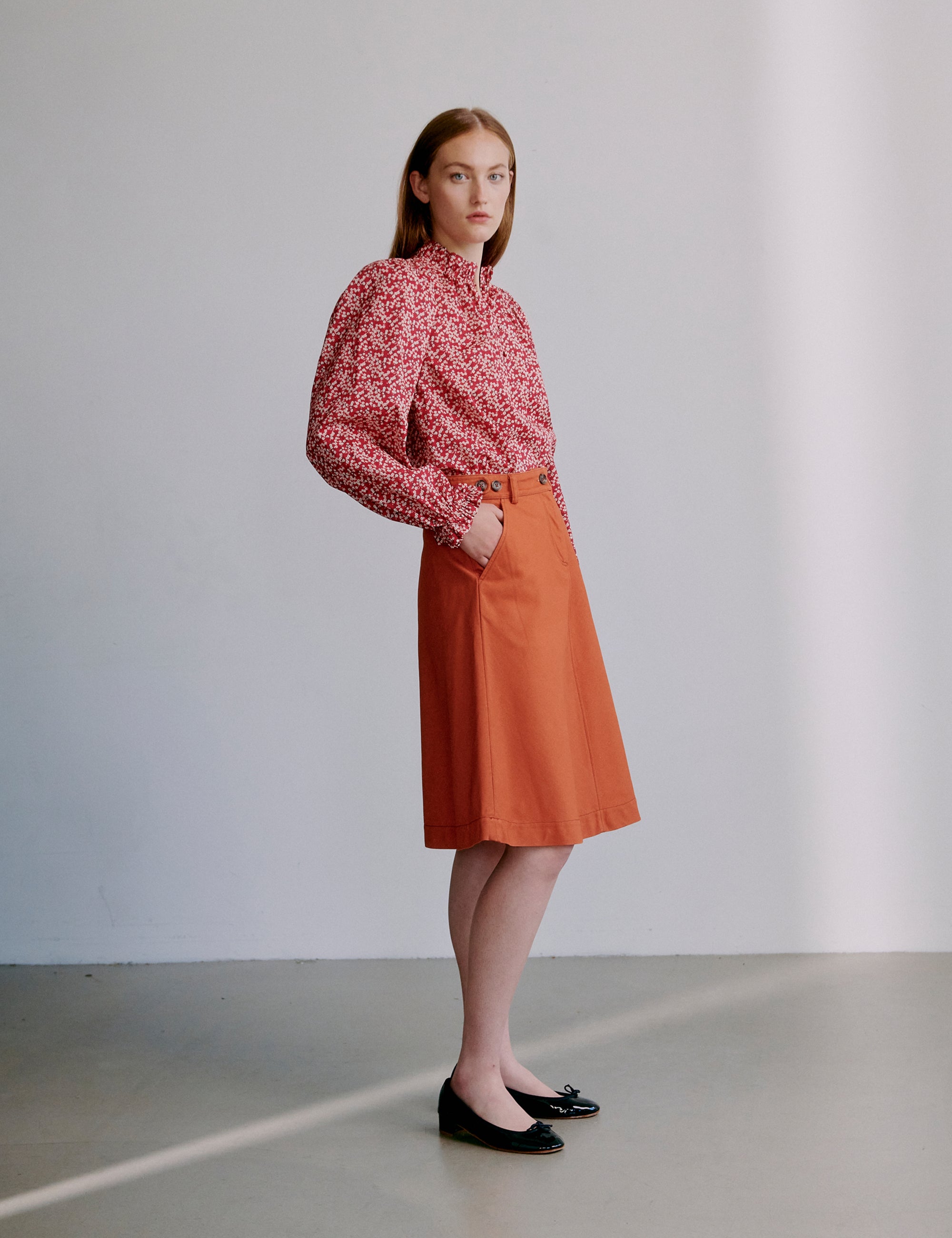 Woman wearing a red floral blouse and orange skirt against a plain background