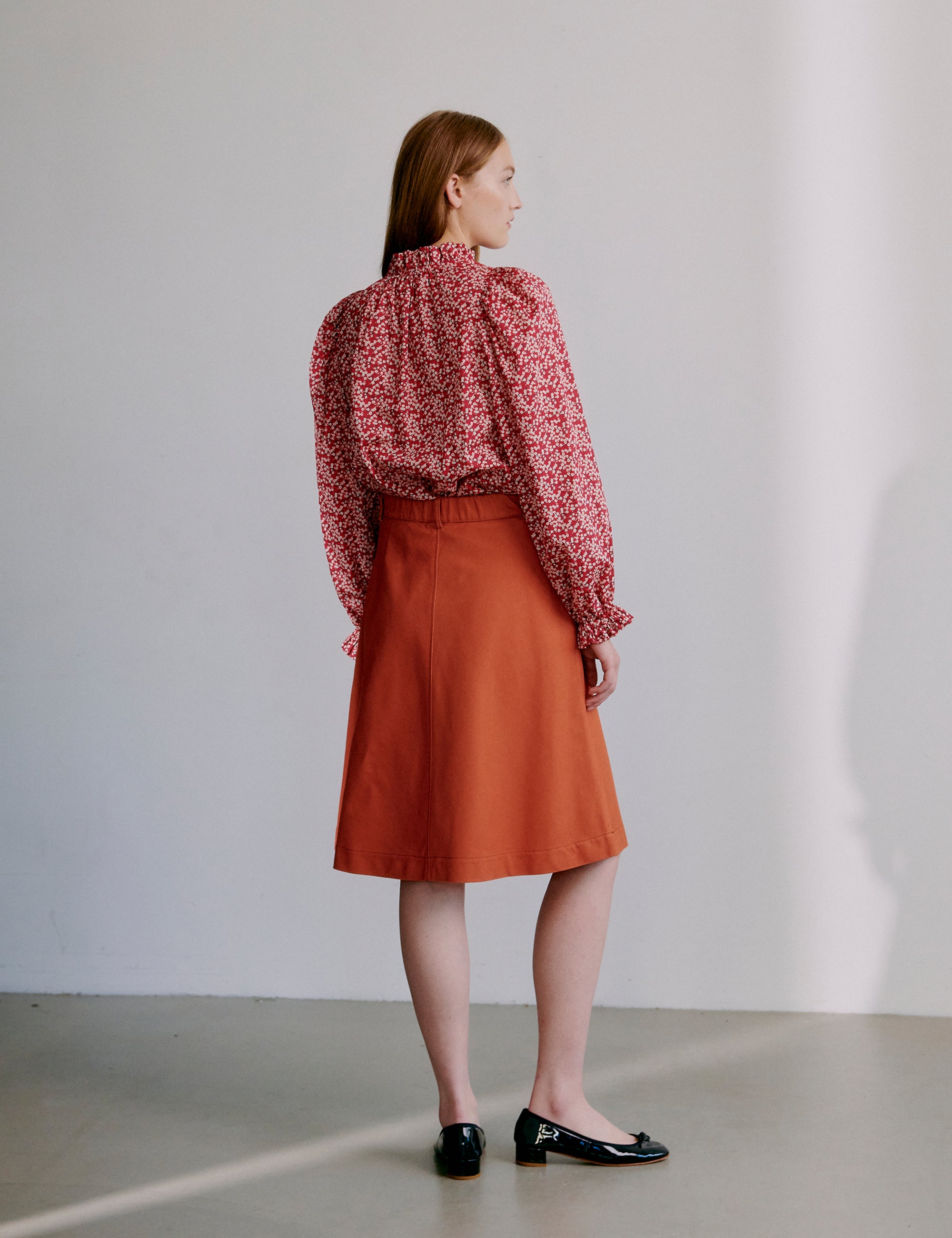 Woman wearing a red floral blouse and orange skirt against a plain background