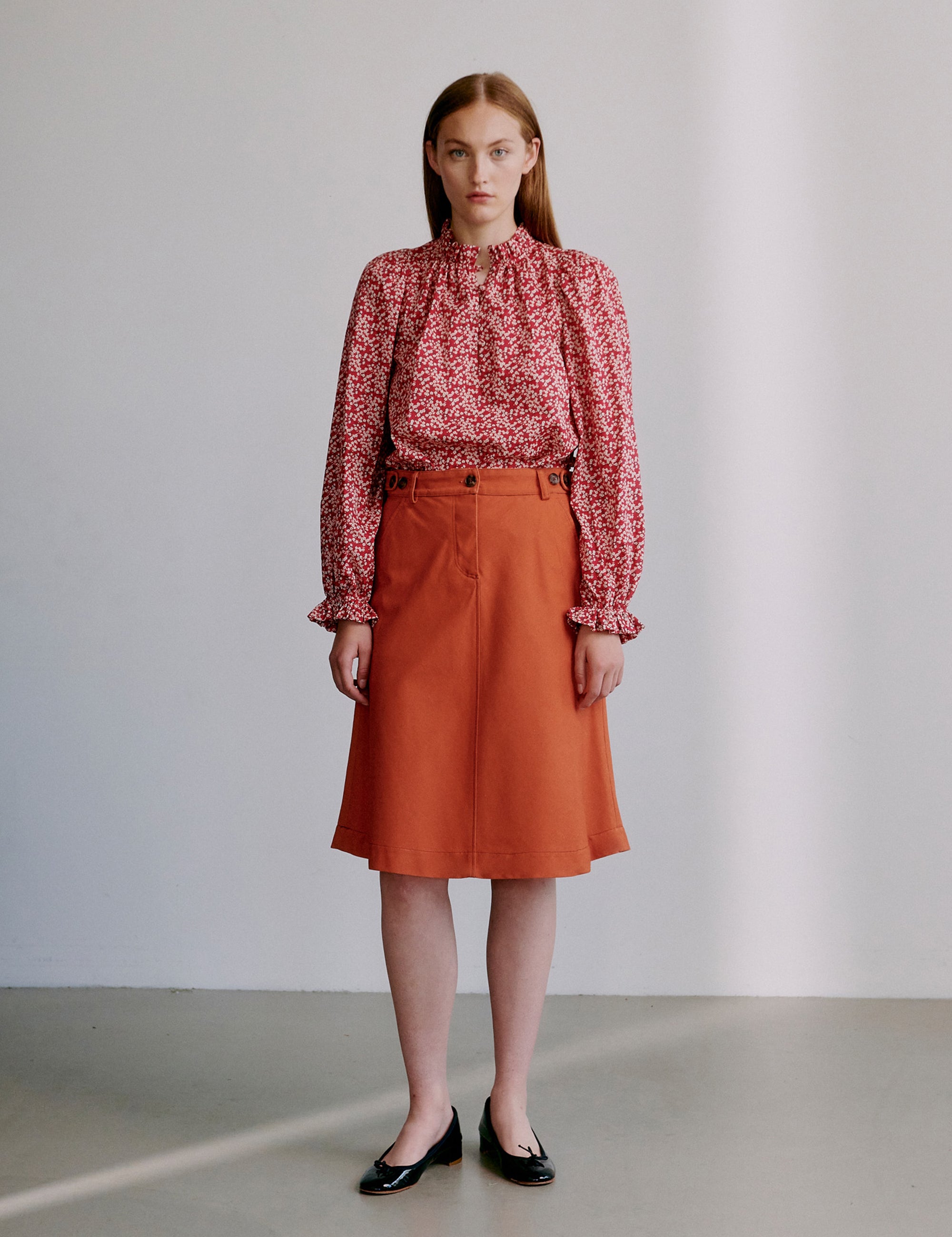 Woman wearing a red floral blouse and orange a-line skirt and black shoes
