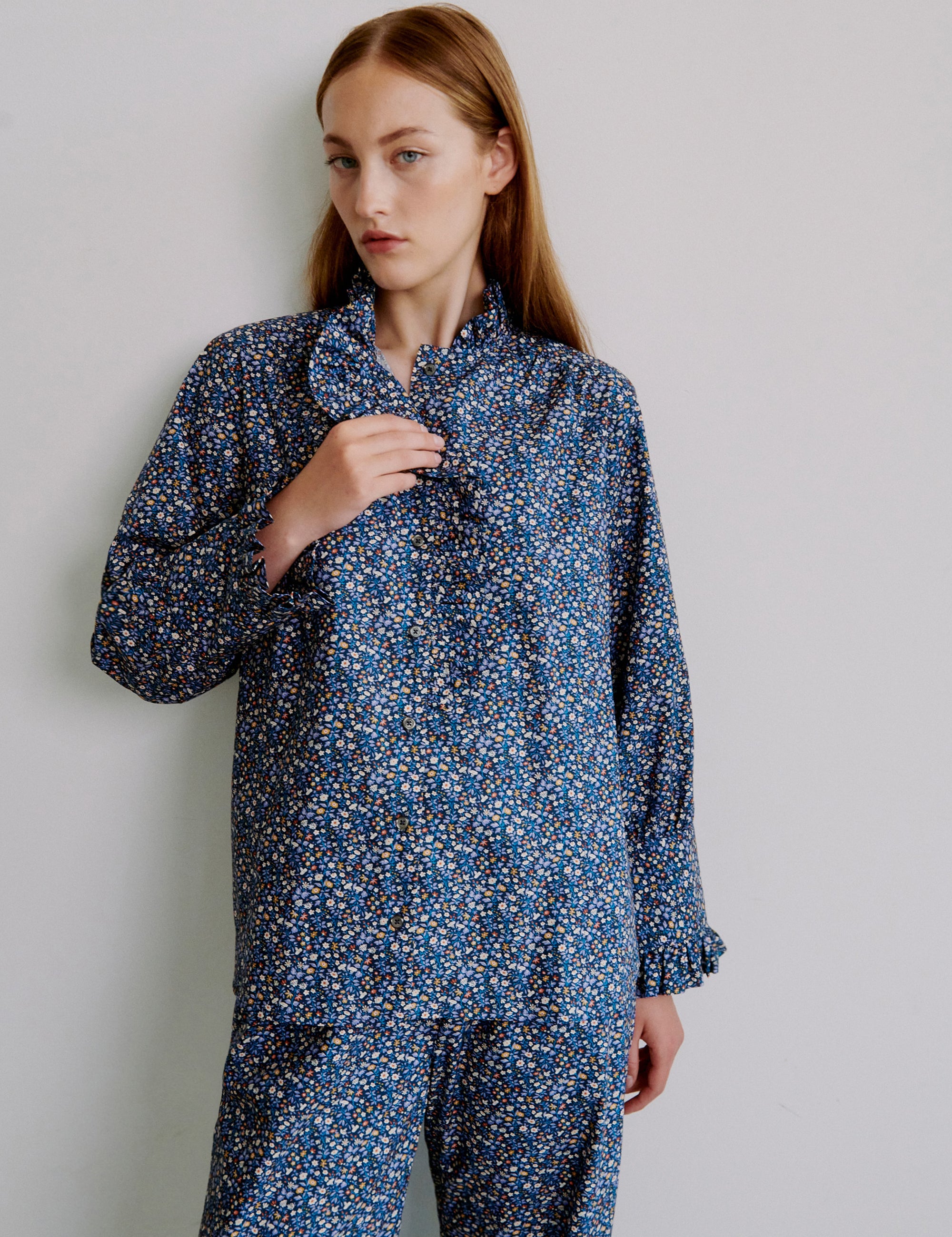 Kvinna i blå blommig outfit med långärmad volangskjorta och byxor