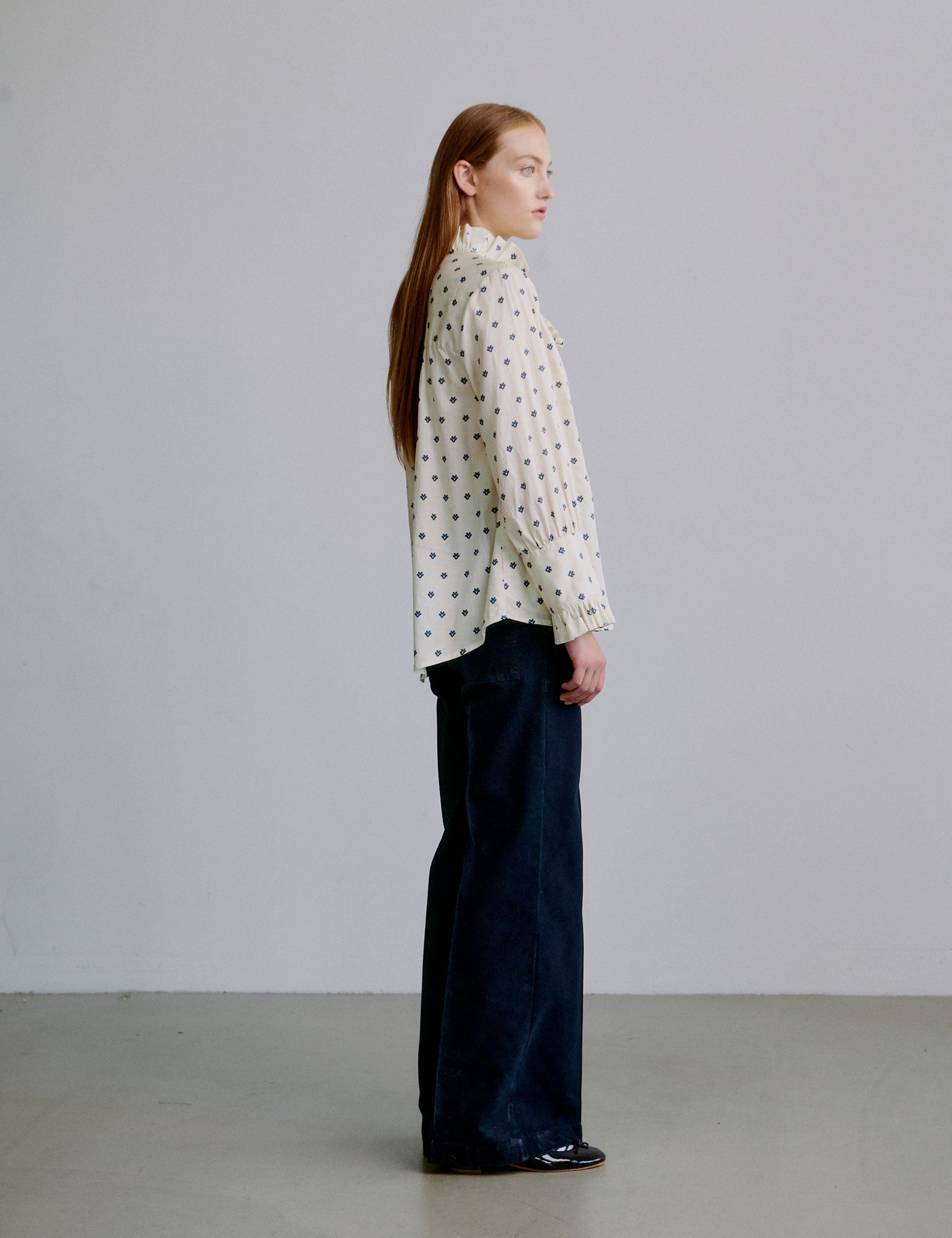Woman wearing a polka dot blouse and dark blue wide pants against a plain background