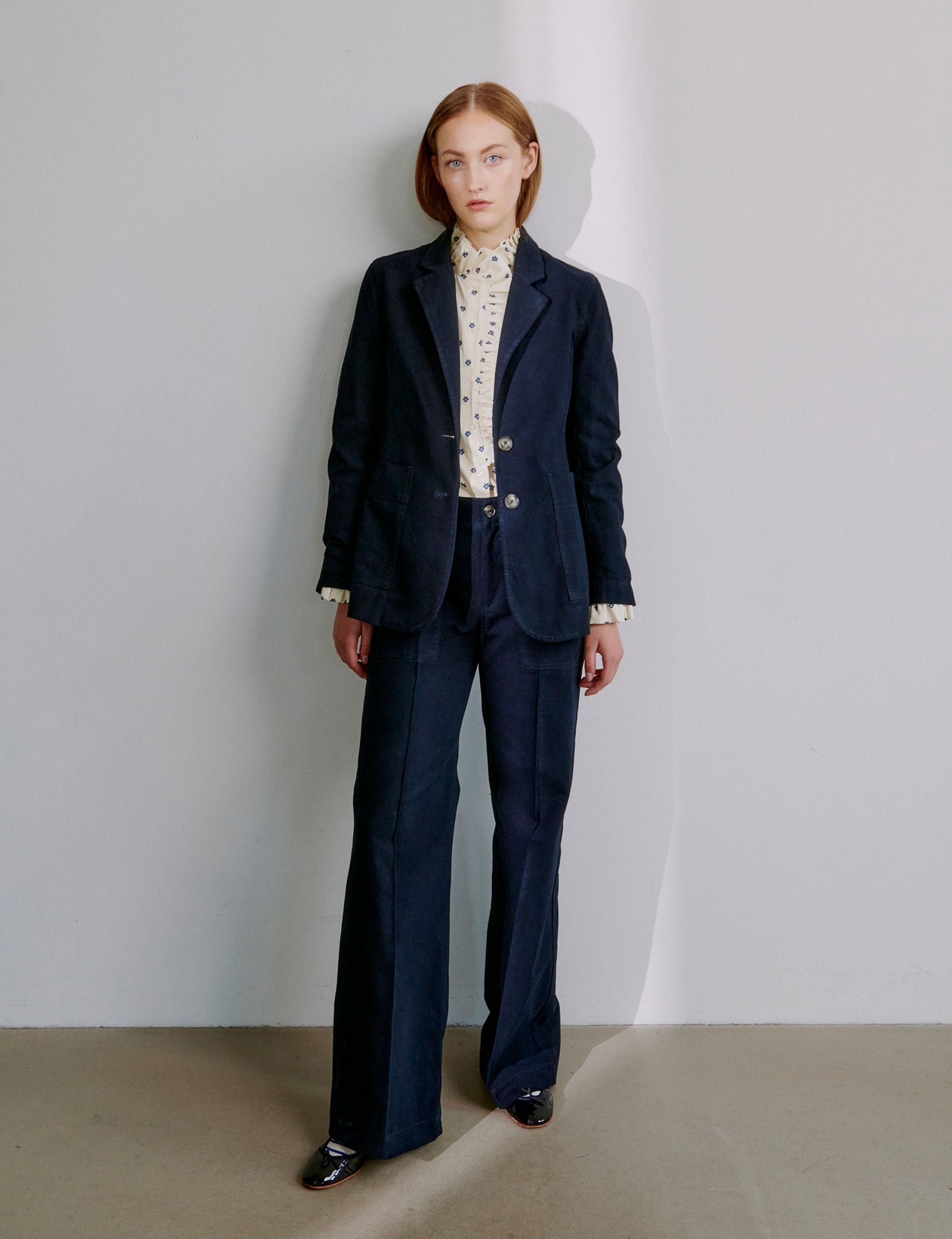 Woman wearing a navy blue suit with a white dotted shirt against a plain background