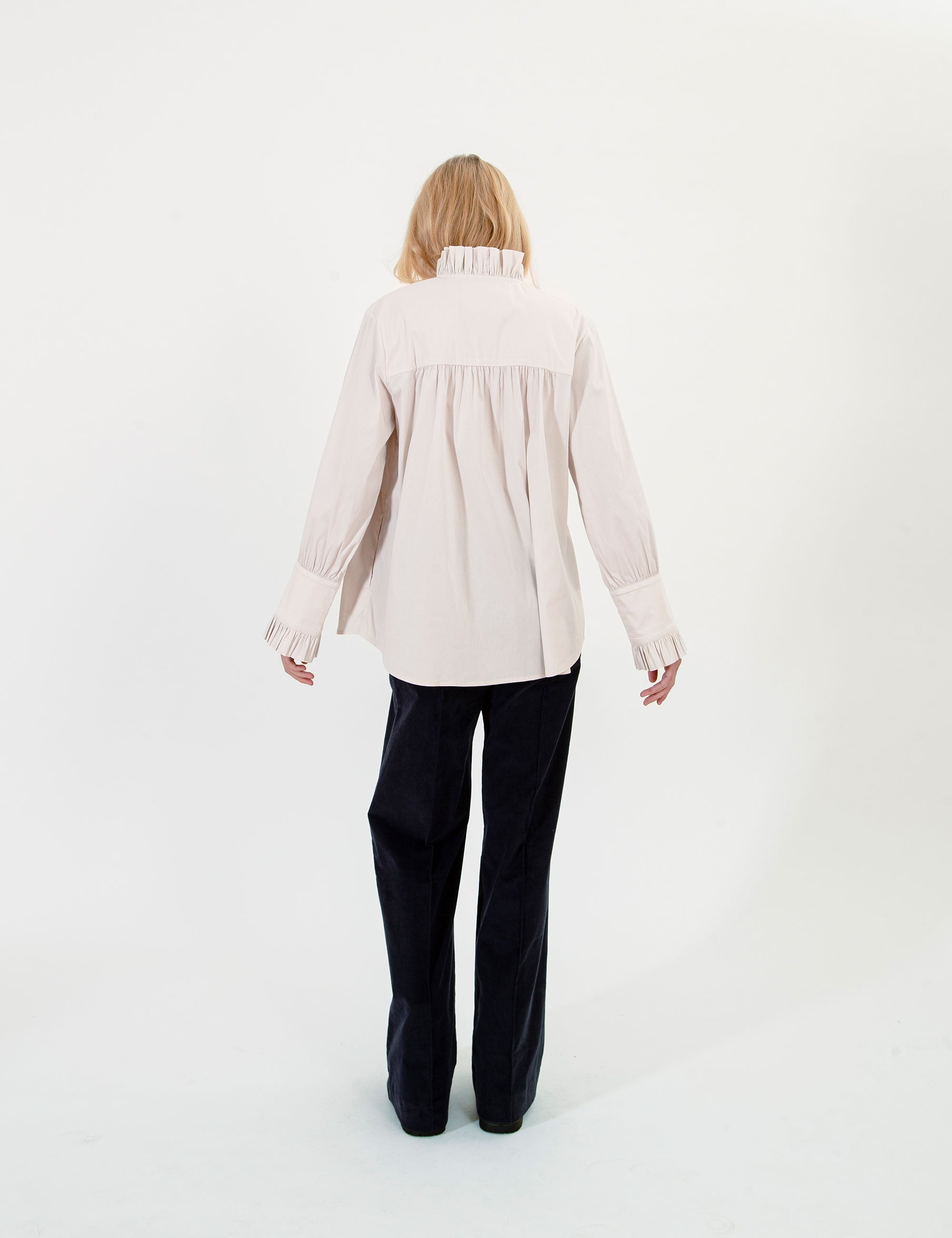Woman wearing a light-colored ruffled blouse and dark pants on a white background