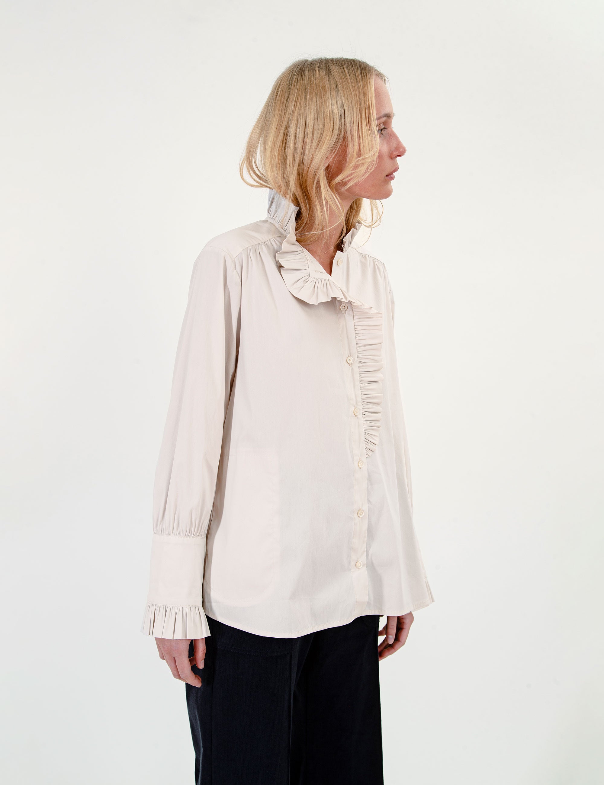 Woman wearing a light-colored ruffled blouse and dark pants on a white background