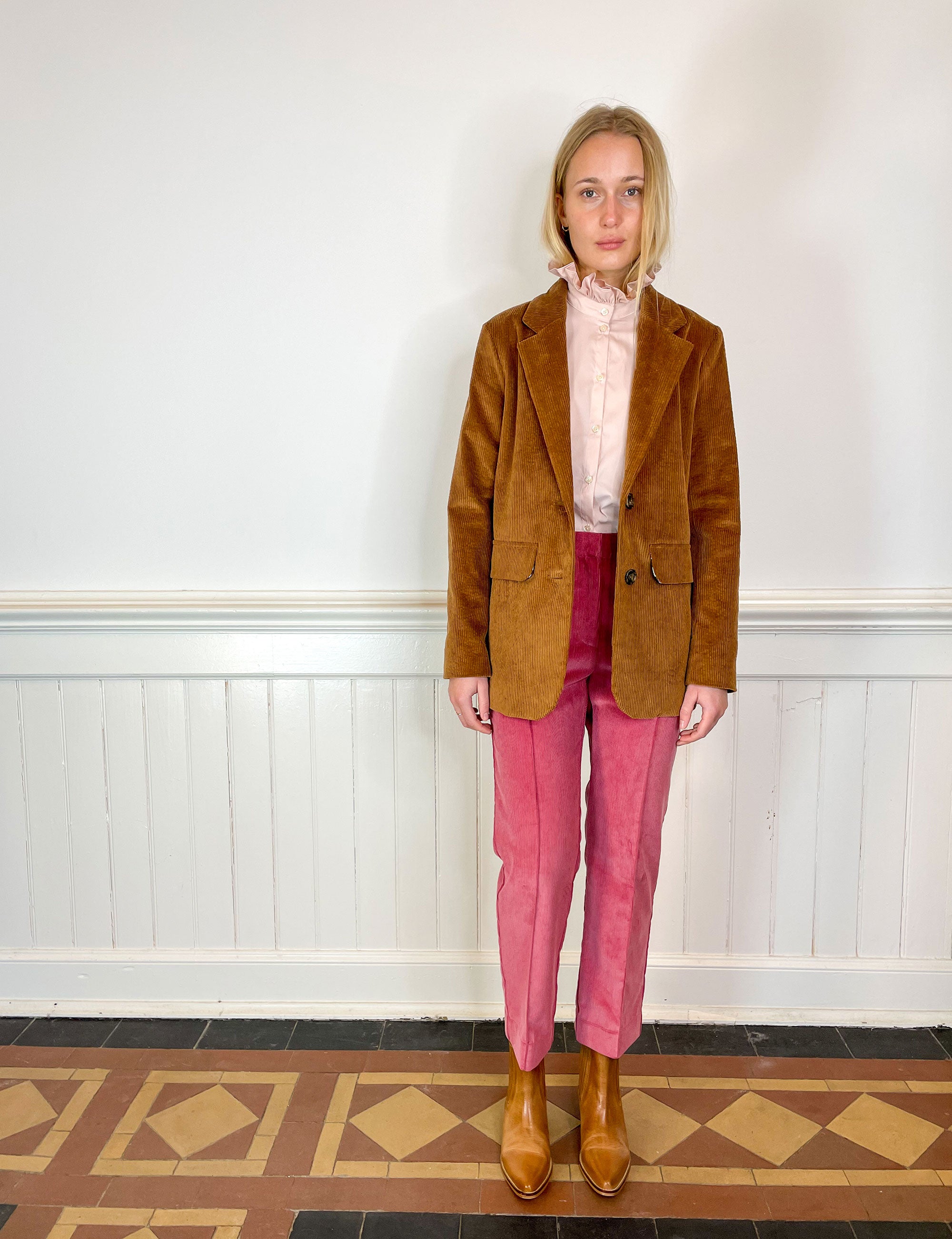 Woman in dusty rose corduroy pants, pink shirt with frilled collar and brown corduroy jacket