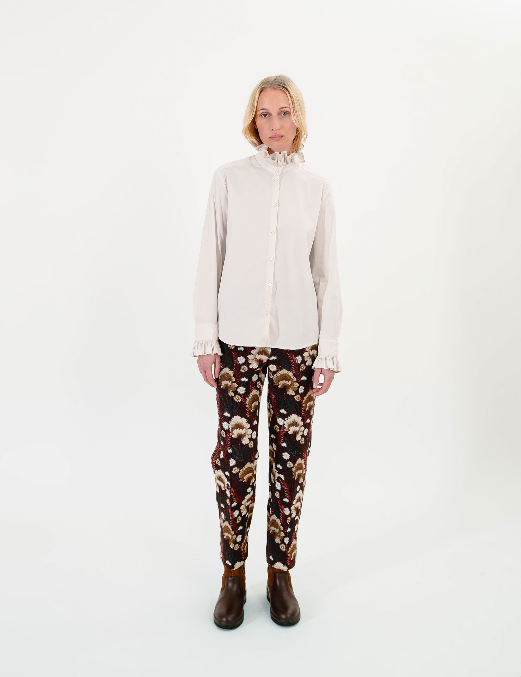 Woman wearing a cream blouse and brown patterned pants on a white background
