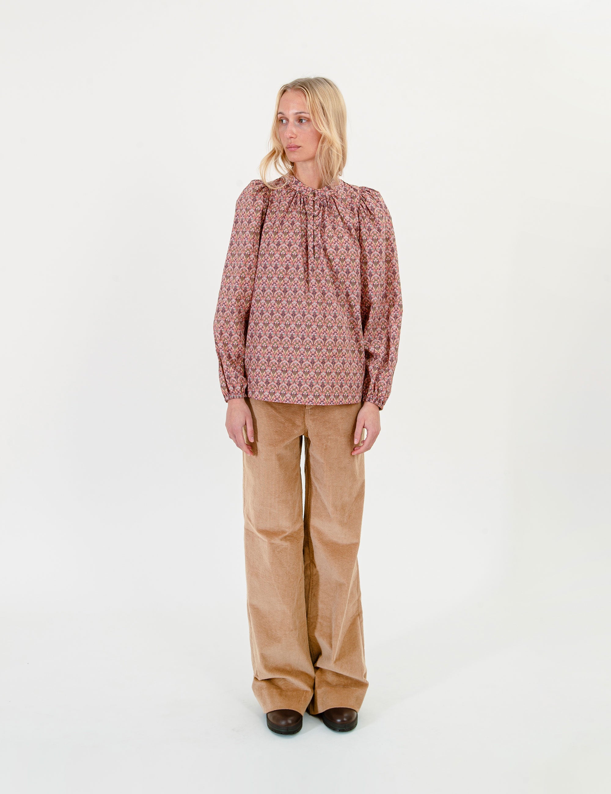 Woman wearing a patterned blouse and beige corduroy pants on a white background