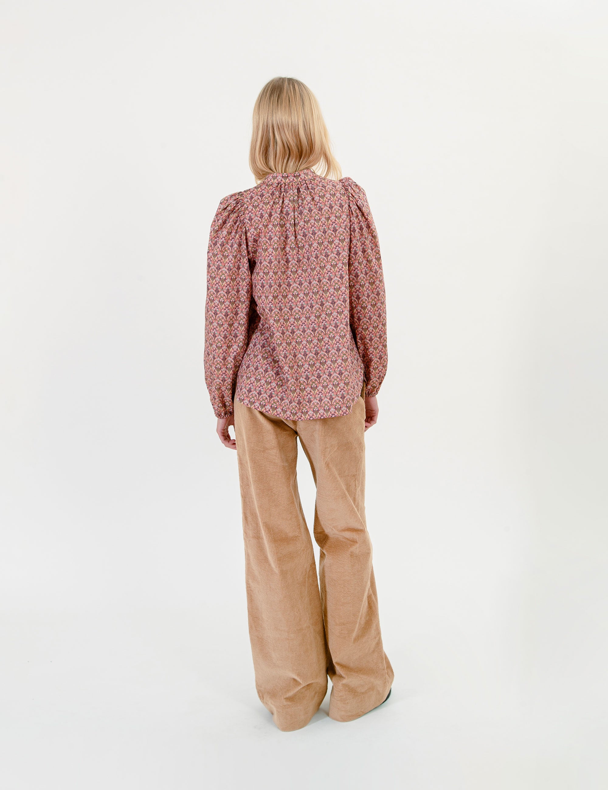 Woman wearing a floral patterned blouse and beige corduroy pants on a white background