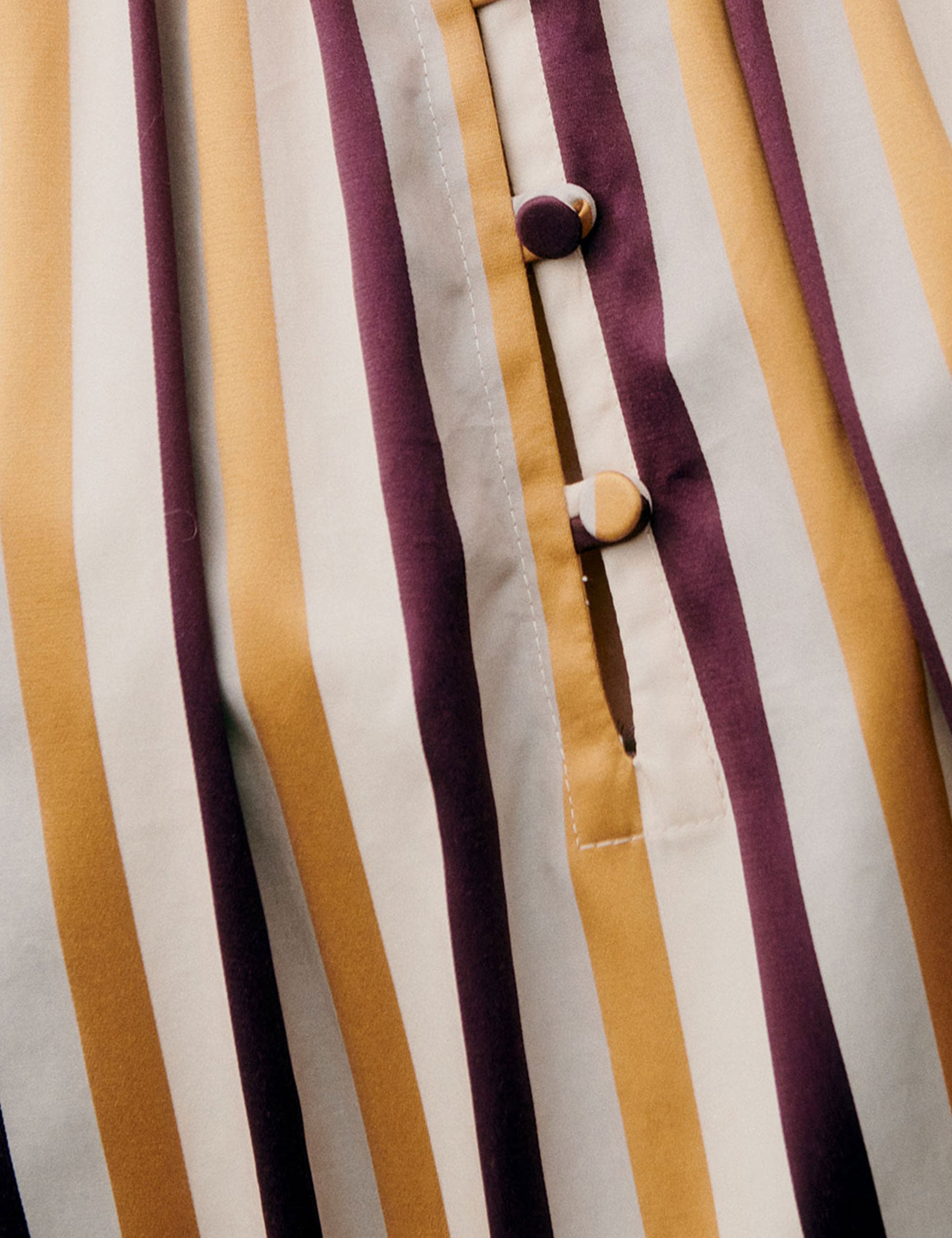 Detailed close-up of buttons and vertical stripes on fabric in yellow, purple, and white