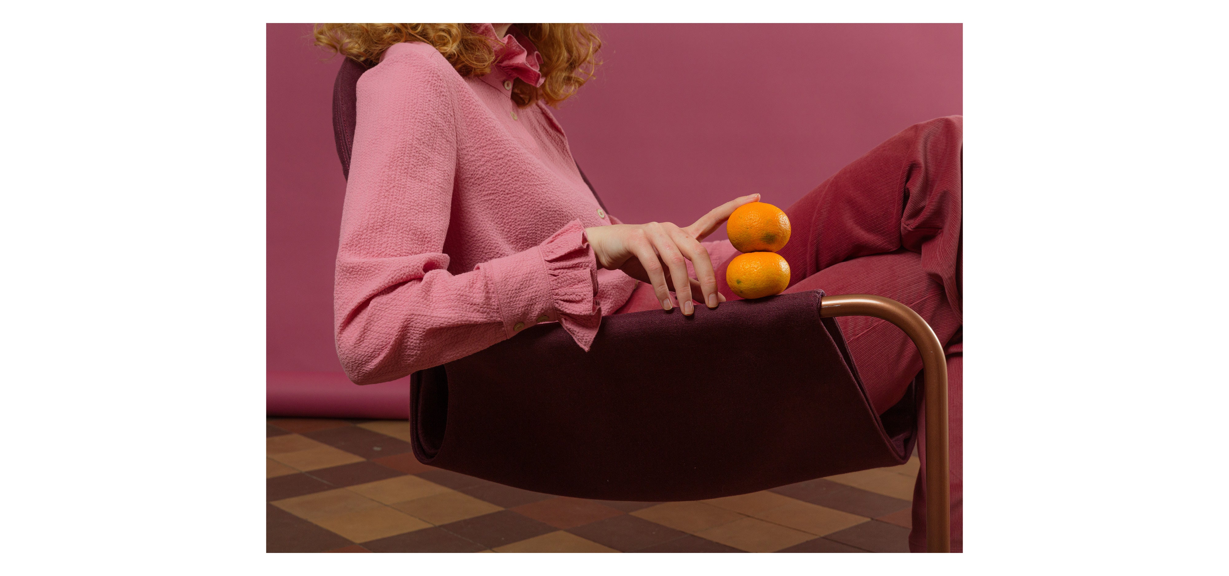 Woman sitting in chair wearing red pants and pink shirt with frilled cuffs