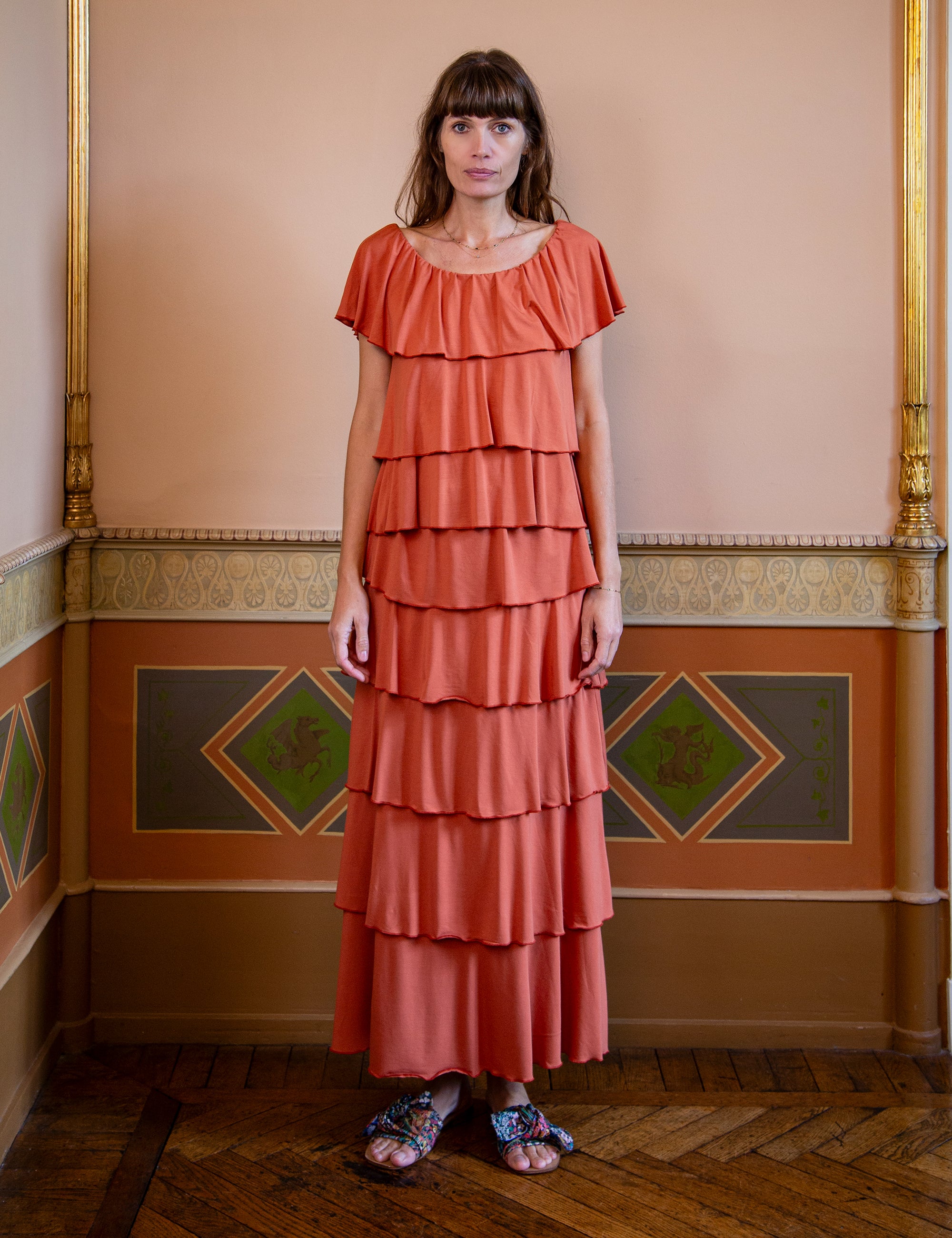 Woman wearing a coral tiered top and skirt in an ornate room.