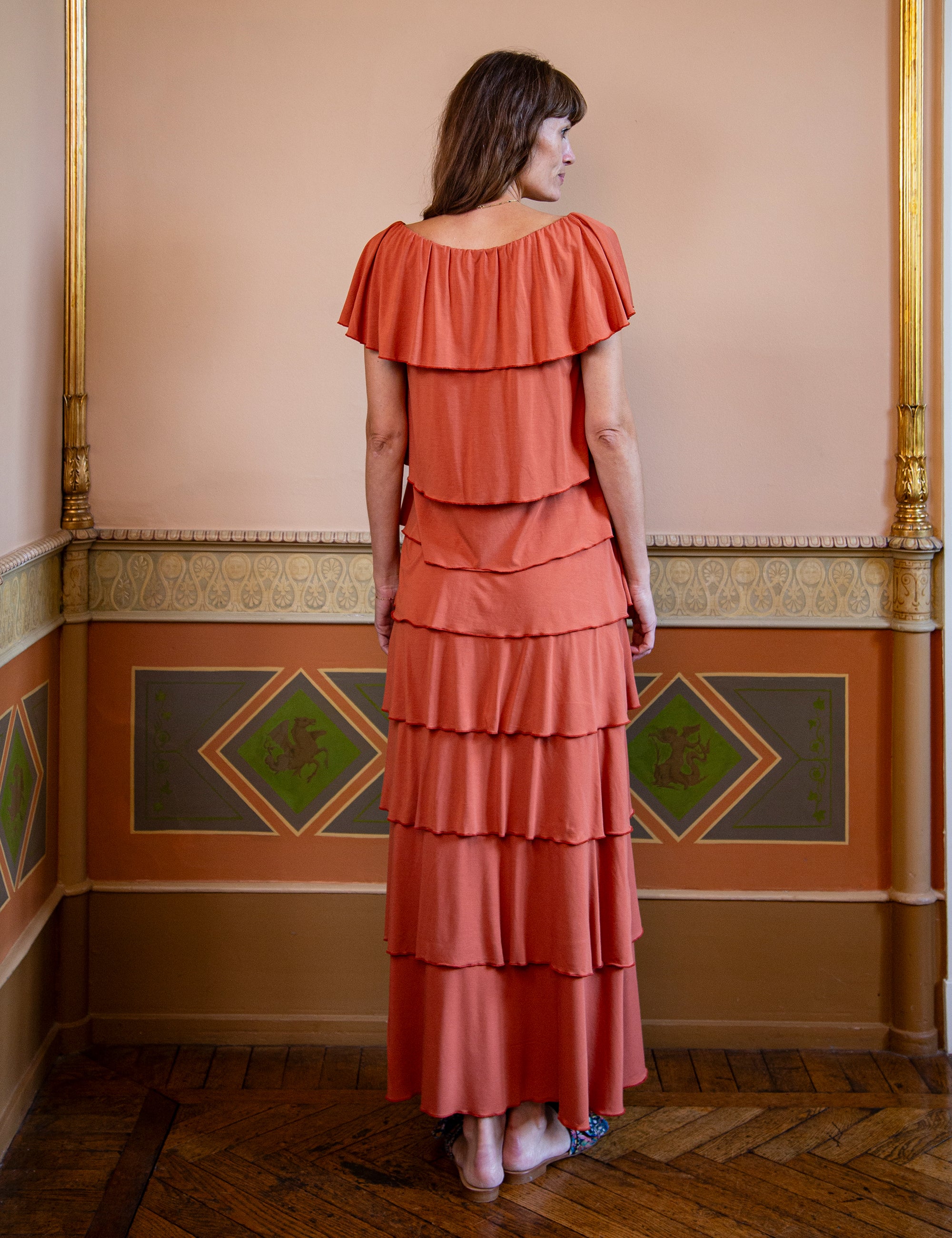 Woman wearing a coral tiered top and skirt in an ornate room.