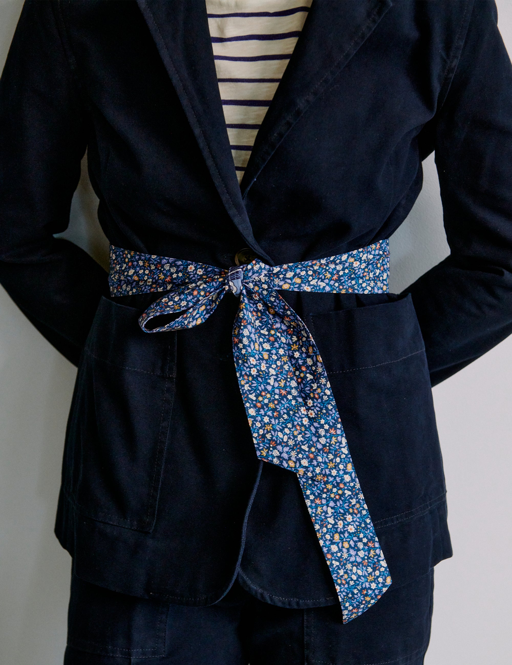 Navy blue jacket with a blue floral fabric belt tied around the waist on a plain background
