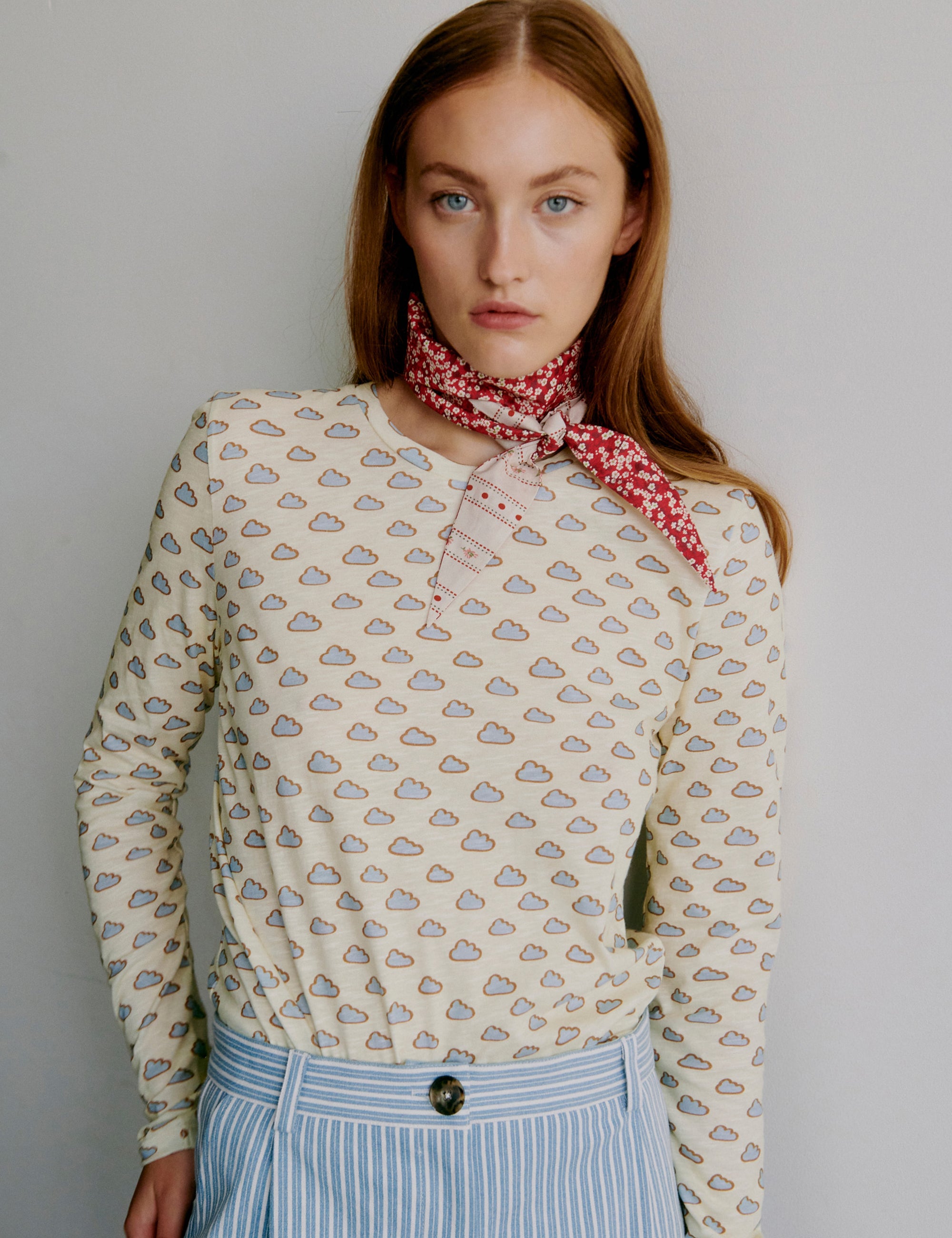 Woman wearing a cloud patterned t-shirt, red flower patterned scarf and blue and white striped pants