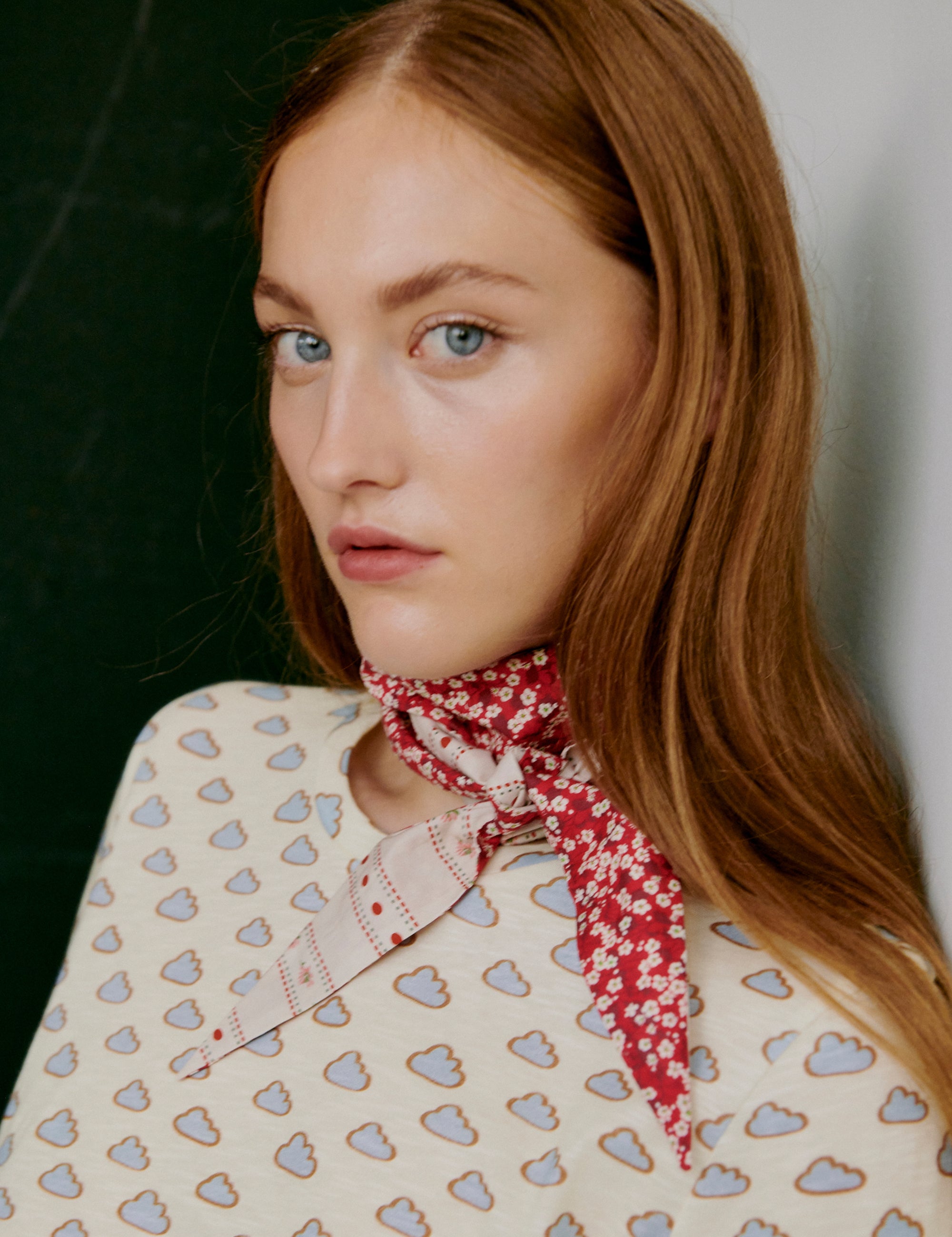 Woman wearing a cloud patterned t-shirt and red flower patterned scarf against a neutral background